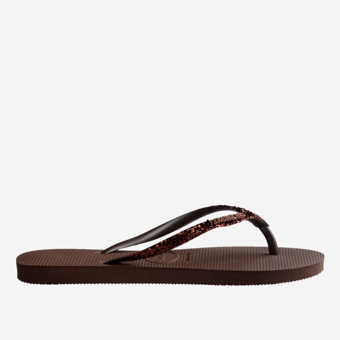 Sandalias de la marca Havaianas, modelo SLIM GLITTER. Chancas elaboradas en plástico color marrón. Chanchas con ligereza, la suela de foma suave acompaña el pie sin pesar y el acabado antideslizante te da seguridad tanto en la arena como en el paseo de la tarde. El diseño se centra en estilizar el pie con unas tiras finas con glitter que aportan un brillo discreto y muy favorecedor. Cada detalle está pensado para que las chanclas Havaianas SLIM GLITTER funcionen como una extensión natural de tu estilo: limpias, depuradas y con ese punto elegante que diferencia unas chanclas premium de unas básicas.