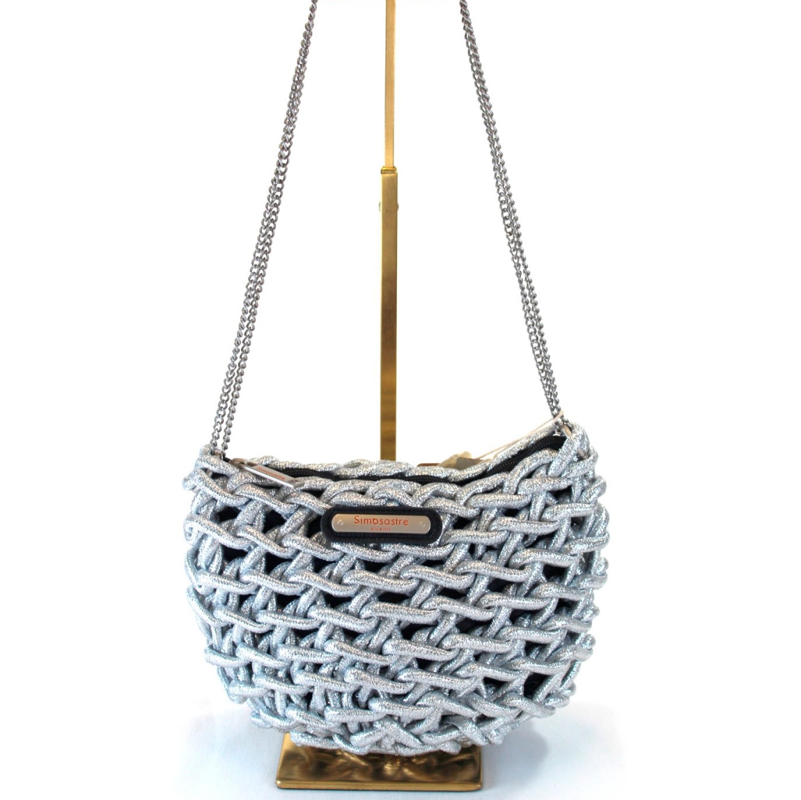 Bolso de la marca Simosastre, modelo JANETH. Bolso cruzado de cuerda elaborado en tela color plata con logo de acero en parte frontal. Cierre del bolso con cremallera y bandolera en metal en oro. Medidas del bolso:a lto 17cm y ancho 23cm. Este bolso Simosastre JANETH es un complemento ieal para darle estilo y personalidad a tus looks de temporada.