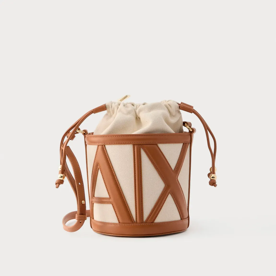 Bolso tipo cubo de la marca Armani Exchange, modelo RACHEL. Bolso elaborado en polipiel color cuero. Tiene una silueta depurada, definida por líneas suaves y una paleta de colores neutros, se presta a innumerables combinaciones de estilo, con logo en todo el bolso. Con asas extraíbles de hombro. Bolso Armani Exchange RACHEL, un accesorio imprescindible para la mujer moderna que busca un toque de lujo discreto, perfecto para guardar sus secretos cotidianos con elegancia y sofisticación.