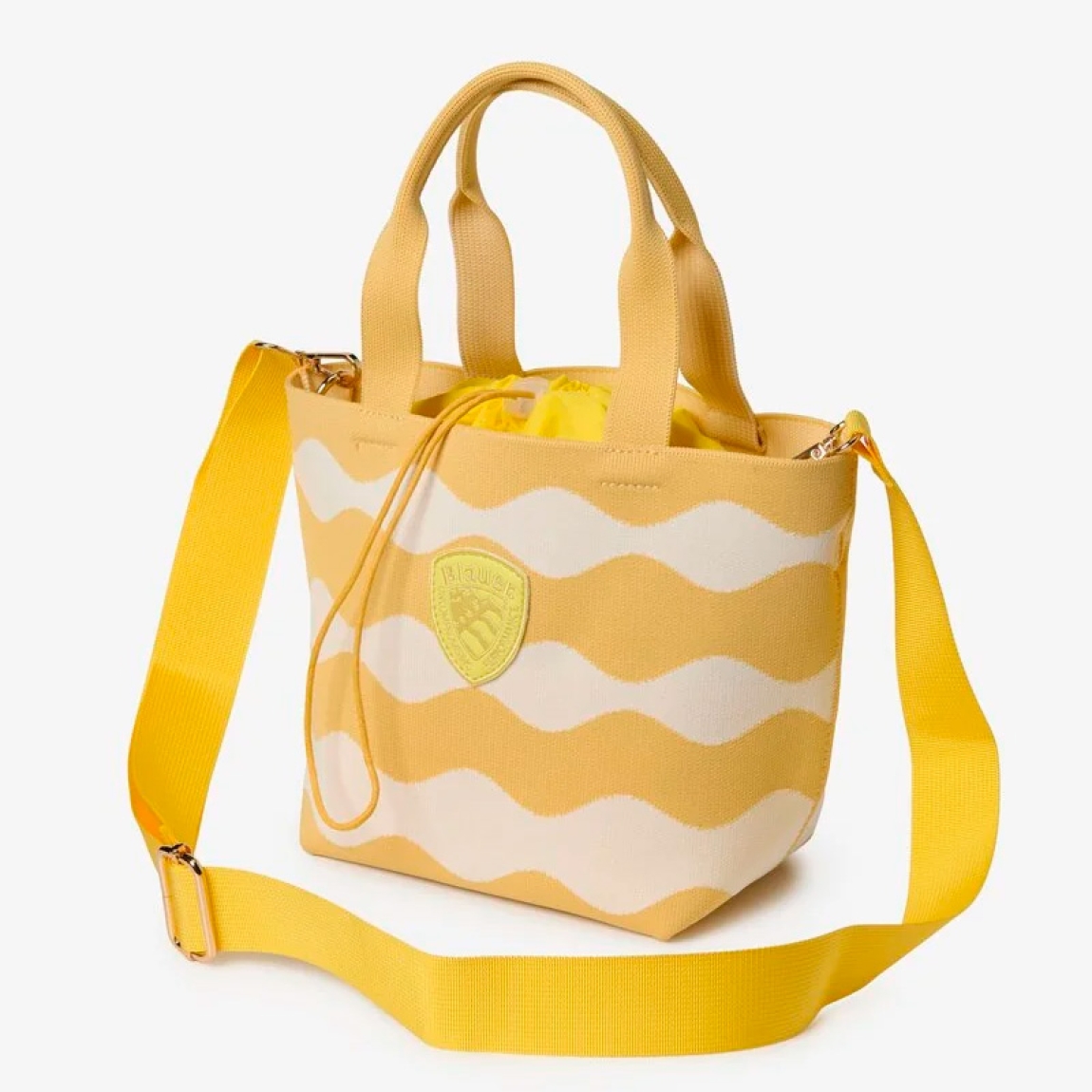 Bolso de la marca Blauer, modelo BASK. Elaborado en tejido técnico color amarillo con un motivo de ondas, combina practicidad y un estilo contemporáneo. Bolso Blauer tipo canasta, es el accesorio ideal para la temporada de calor. Bolso Blauer dispone de dobles asas resistentes y el icónico escudo logotipado en el frontal. Ideal para el ocio o una jornada en la playa con un toque chic. Bolso Blauer BASK, ideal para llevar a todos lados! Medidas: 20 x 18 x 12cm.