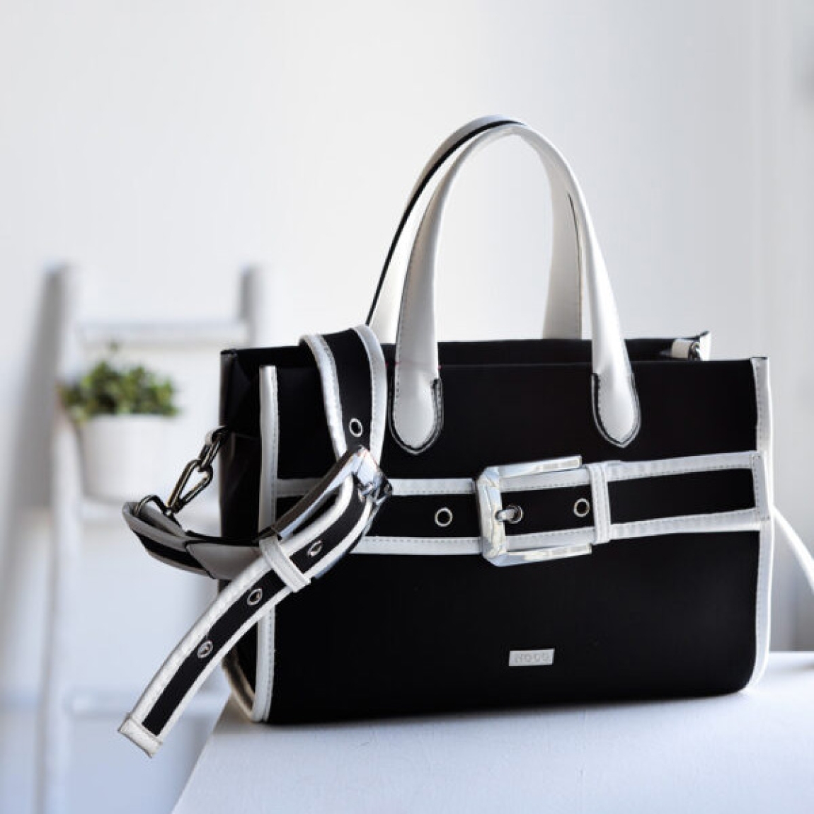 Bolso clásico de la marca Noco, modelo TORI. Elaborado en neopreno color negro con detalle en blanco. Hebilla en parte frontal del bolso. Cierre con cremallera y tiene dos asas para llevar de mano y una larga regulable. Medidas: alto 20cm y ancho 28cm. Este bolso Noco TORI tiene el tamaño mediano perfecto para quienes necesitan un bolso espacioso pero no demasiado grande. Bolso ligero y resistente.
