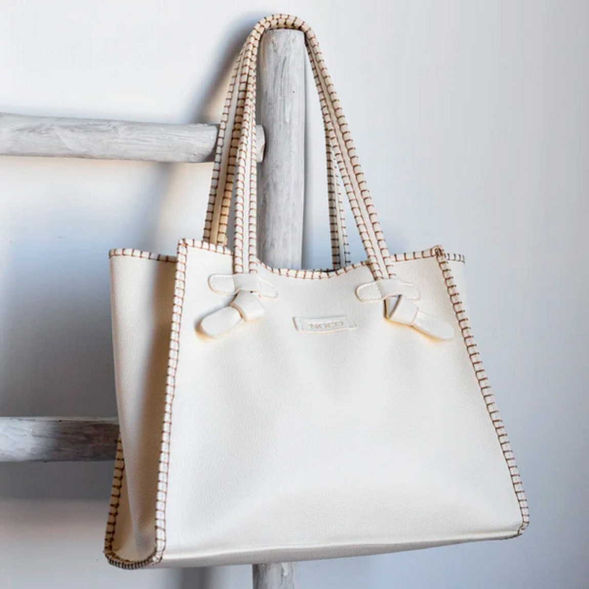 Bolso shopper Noco, modelo SHANON. Elaborado de piel vegana color blanco. Este bolso es una pieza única que combina estilo y sostenibilidad. Su formato se distingue por su trabajo de diseño original, aportando una forma sofisticada y funcional. El material de piel vegana tiene un acabado que imita a la perfección la piel real, con un suave interior similar al pelo característico de la piel auténtica, brindando una textura premium. Cierre con boton. Medidas alto 26cm y ancho 30cm.