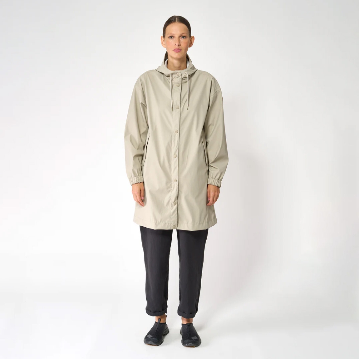 Chaqueta impermeable de la marca Tanta, modelo Mis. Es un chubasquero de corte holgado y diseño siempre contemporáneo 100% impermeable. Está confeccionada con un tejido ligero de PU color beig y cuenta con todas las costuras selladas para una protección superior. Los detalles de la prenda incluyen botones a presión, una capucha con visera incorporada y bolsillos con ribetes. Ideal para esta temporada!
