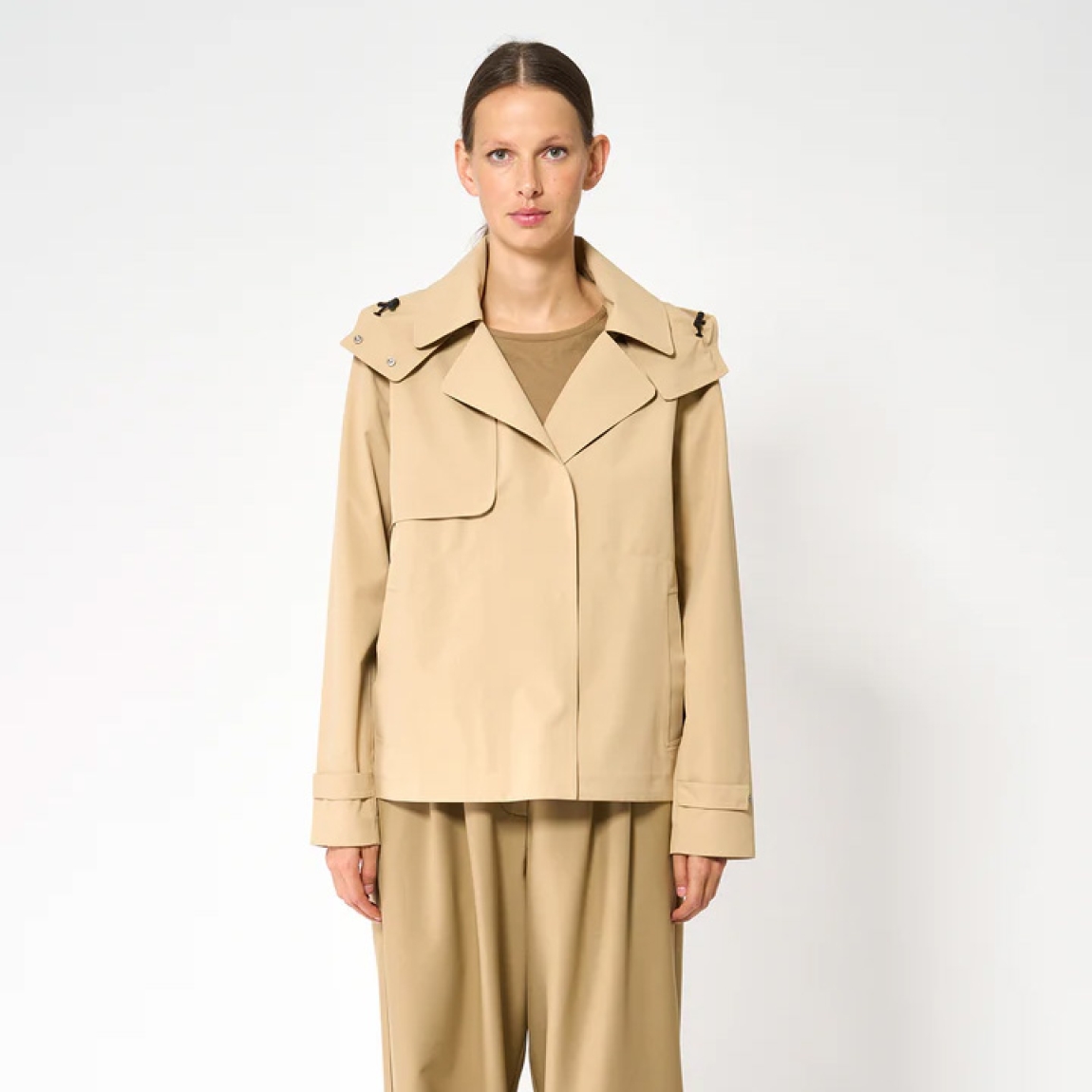 El trench o gabardina corta impermeable de la marca Tanta, modelo NIWL está cofeccionado en tejido de sarga de poliéster color camel. Es 100% impermeable y cuenta con todas las costuras selladas para una protección superior.Los detalles de la prenda incluyen un canesú en la espalda y otro en el lado derecho de la parte delantera, botones a presión ocultos y una capucha desmontable con cordón ajustable. Diseñado con un corte impecable, el modelo Niwl combina elegancia con una alta funcionalidad.