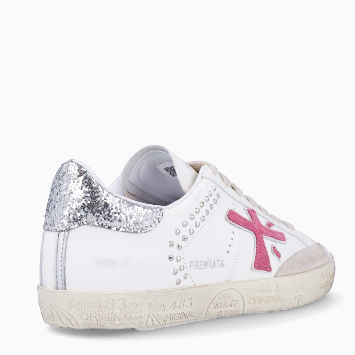 Deportivas de la marca Premiata, modelo STEVEND. Exterior de las deportivas en piel color blanco con detalle en tachuelas y glitter plateado en el talón. Logo de color fucsia. Interior de las deportivas en piel color blanco. Cierre de las deportivas con cordones blancos. Deportivas Premiata Stevend tienen el diseño perfecto para temporada, no puede faltar este modelo clásico en tu armario!