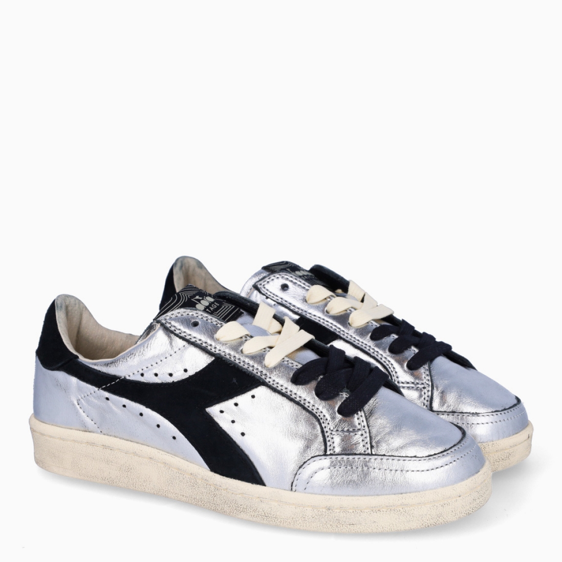 Deportivas de la marca Diadora, modelo ZULE. Exterior en piel color plata con efecto brillante y detalles en negro. Interior en textil color beig con plantilla acolchada y extraíble para máxima comodidad. Cierre con cordones de doble color: negro y beig. Suela de goma con cuña de 2cm de altura. Estas deportivas son unas clásicas ideales para llevar en tu día a día.