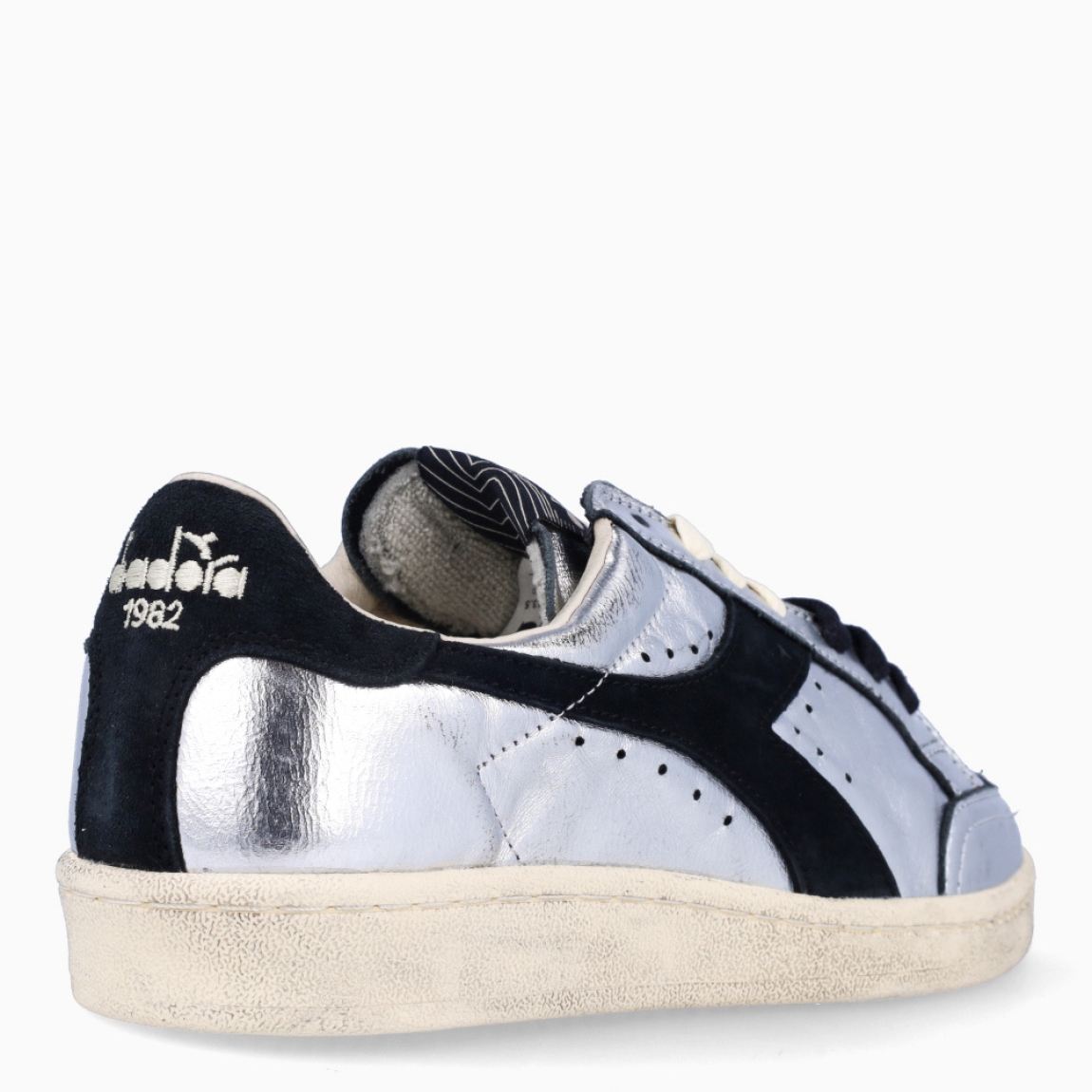 Deportivas de la marca Diadora, modelo ZULE. Exterior en piel color plata con efecto brillante y detalles en negro. Interior en textil color beig con plantilla acolchada y extraíble para máxima comodidad. Cierre con cordones de doble color: negro y beig. Suela de goma con cuña de 2cm de altura. Estas deportivas son unas clásicas ideales para llevar en tu día a día.