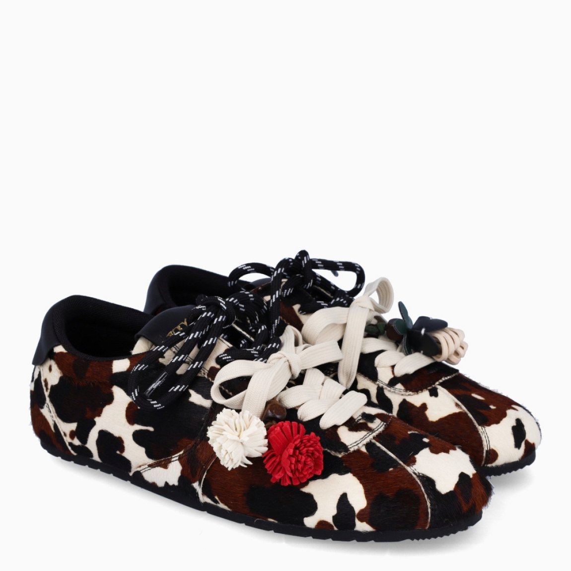 Deportivas de la marca Itse, modelo SALMA. Exterior en pelo con estampado animal print de vaca. Interior en textil color marrón. Cierre con cordones dobles, uno marrón y otro, beig. Deportivas Itse con tres charms sujetados a los cordones en forma de pompones y flor roja. Suela plana y de goma. Estas deportivas Itse Salma son un complemento básico y en tendencia para tus looks!