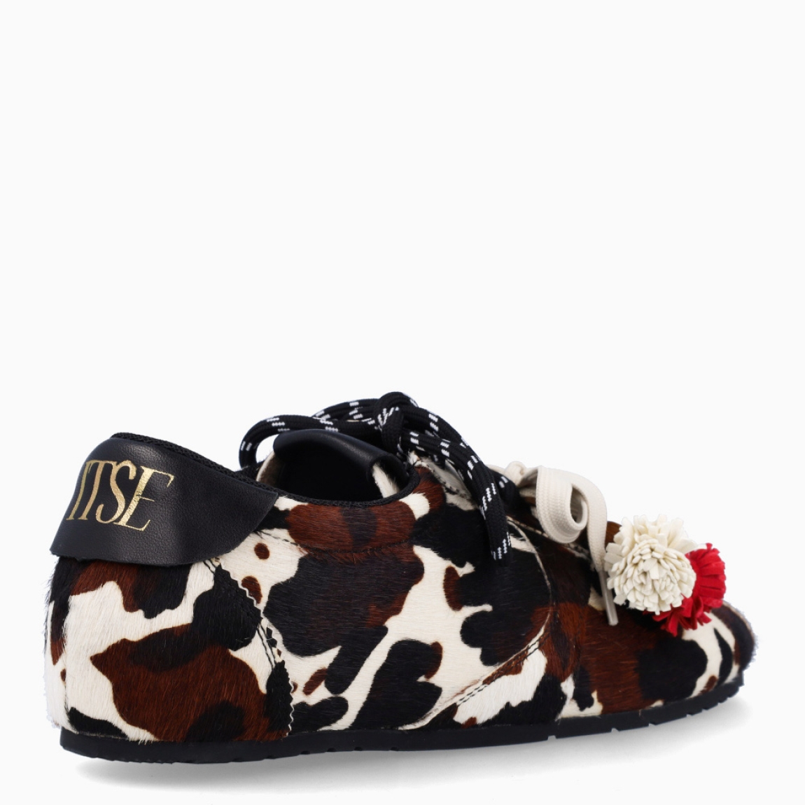 Deportivas de la marca Itse, modelo SALMA. Exterior en pelo con estampado animal print de vaca. Interior en textil color marrón. Cierre con cordones dobles, uno marrón y otro, beig. Deportivas Itse con tres charms sujetados a los cordones en forma de pompones y flor roja. Suela plana y de goma. Estas deportivas Itse Salma son un complemento básico y en tendencia para tus looks!