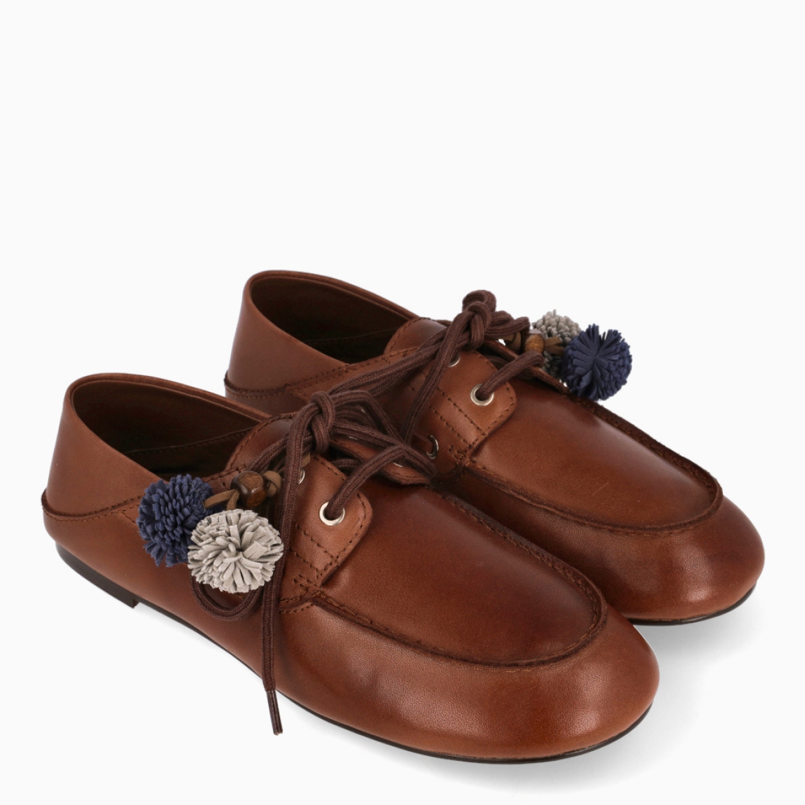 Mocasines destalonados de la marca Itse, modelo SANDRO. Exterior en piel color marrón con detalle de charms colgantes a tono sujetados en cordones color azul y gris. Interior en piel color marrón. Cierre de mocasines con cordones y suela plana de goma. Estos mocasines Itse SANDRO, son un complemento clásico, ideal para crear diferentes looks!