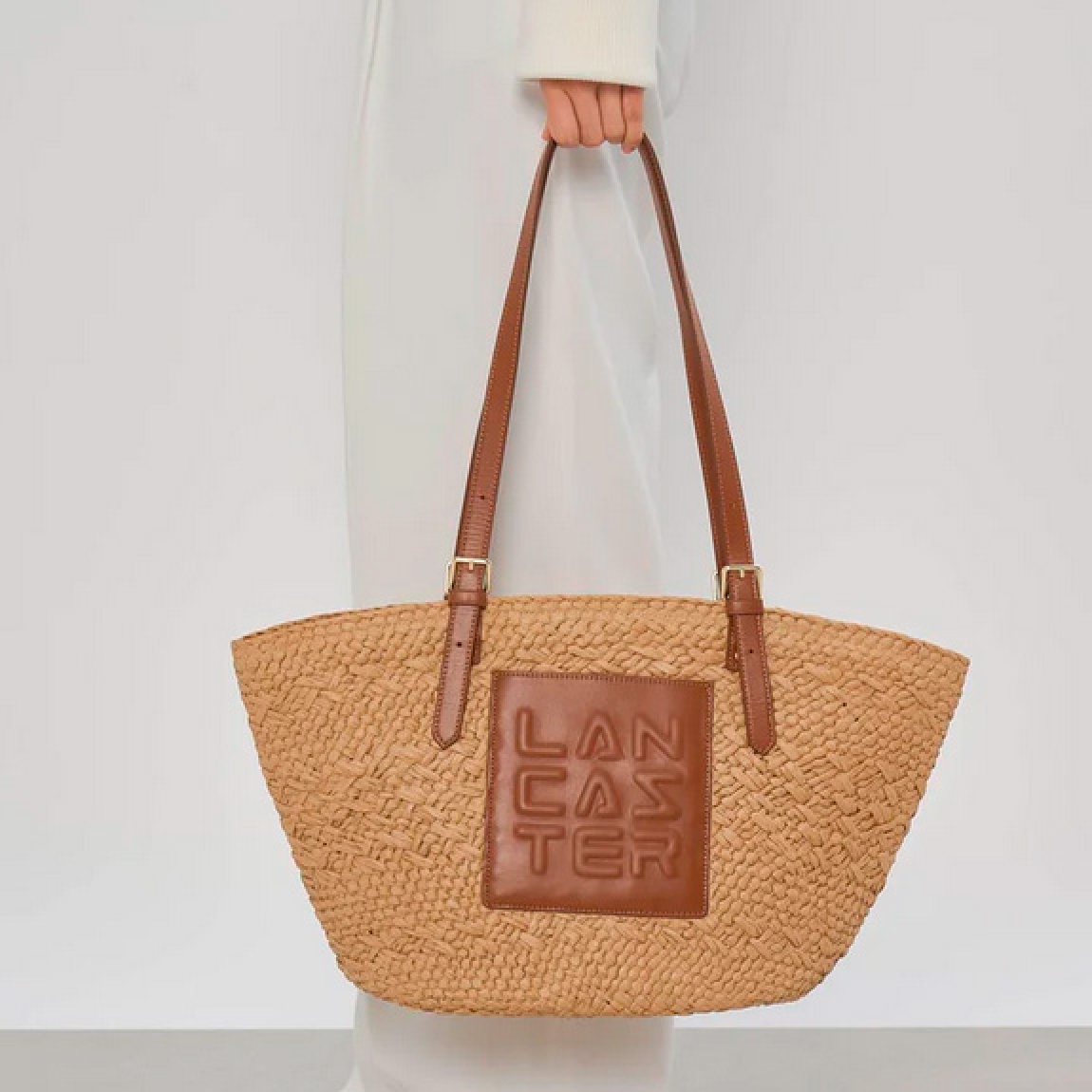 Bolso de la marca Lancaster, modelo ÉPAULEE. Este bolso bandolera está confeccionado en mimbre con guarnición de cuero de vachette color marrón. Su cierre del bolso Lancaste es con cremallera, la cual garantiza el almacenamiento de sus efectos personales, además de un sencillo bolsillo frontal, un sencillo bolsillo interior y un sencillo bolsillo interior doble. Diseñado para una cartera, con un estilo natural y practicidad para el día a día. Medidas: alto 26cm y ancho 45cm.