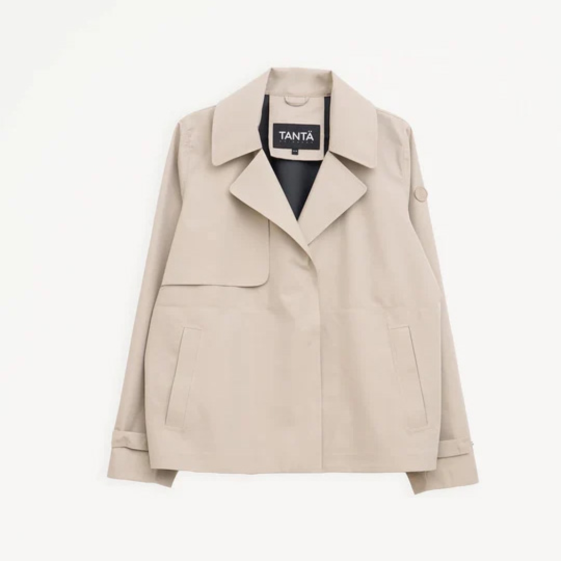 Chaqueta corta impermeable de la marca Tanta, modelo NIWL. Chaqueta sin costuras Niwl está confeccionado en tejido de sarga de poliéster color beig. Es 100% impermeable y cuenta con todas las costuras selladas para una protección superior. Los detalles de la prenda incluyen un canesú en la espalda y otro en el lado derecho de la parte delantera, botones a presión ocultos y una capucha desmontable con cordón ajustable. Diseñado con un corte impecable, esta chaqueta Tanta, modelo Niwl combina elegancia con una alta funcionalidad.
