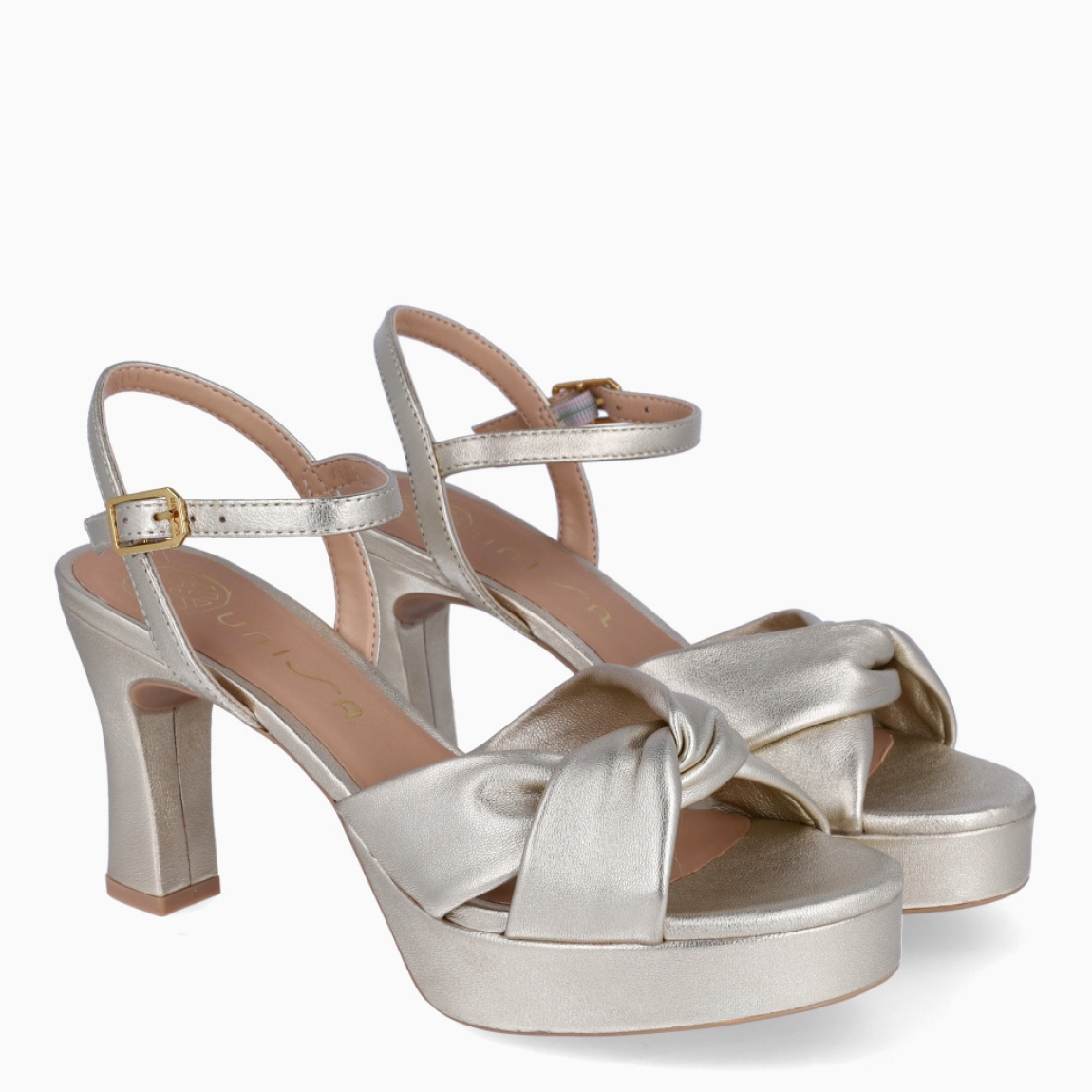 Sandalias de la marca Unisa, modelo ONOA. Exterior en piel color platino con pala cruzada. Interior en piel color nude. Cierre de sandalias Unisa con hebilla en tobillo y un tacón de 8cm de altura. Estas sandalias Unisa ONOA son un complemento clásico e ideal para lucir tus looks de esta temporada!