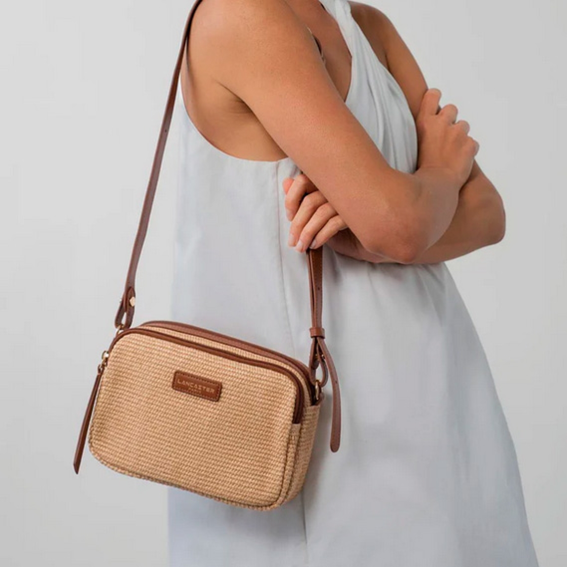 Bolso bandolera de la marca Lancaster, modelo Mini Osier. Este bolso está confeccionado en polipropileno con detalles de piel de vacuno color marrón. Cuenta con un bolsillo frontal con cremallera, un bolsillo interior con cremallera y un bolsillo interior simple. Se lleva al hombro o cruzado. Bolso Lancaster Mini Osier ideal para llevarlo en tu día a día esta temporada. Medidas: alto 15cm y ancho 22cm.