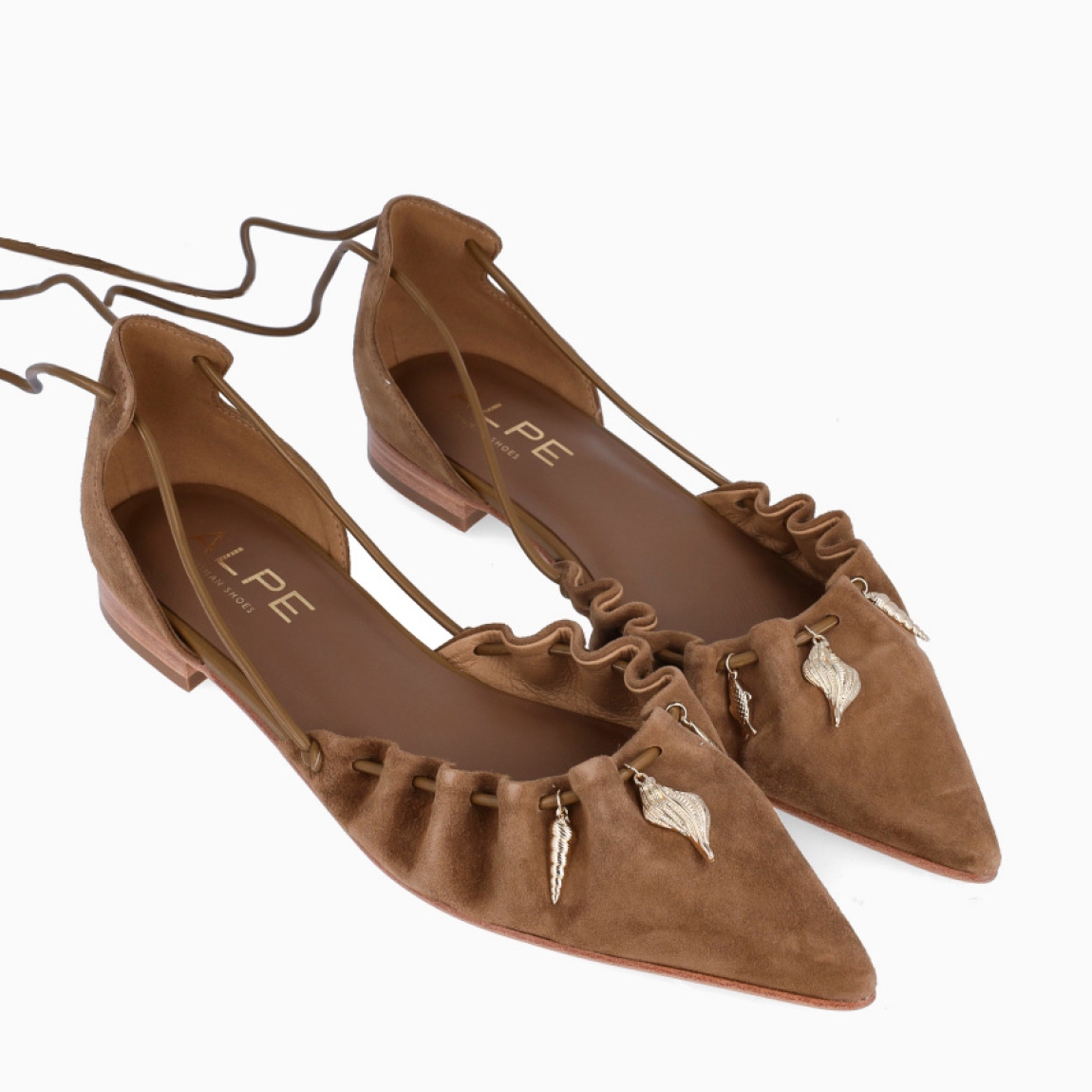 Salones de la marca Alpe, modelo TAMARA. Elaborados en ante color cuero con punta lápiz con efecto corrugada y detalle de dijes dorados colgantes. Interior en piel color cuero. Salones Alpe con cierre de cuerdas largas para amarrar. Salones con suela plana de goma. Estos salones Alpe TAMARA, son un complemento ideal para marcar un estilo único, refinado y cómodo!