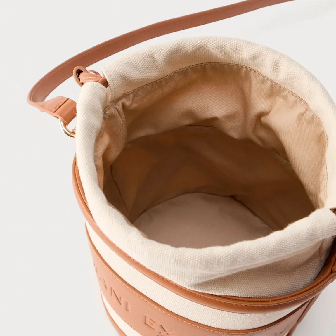 Bolso tipo cubo de la marca Armani Exchange, modelo RACHEL. Bolso elaborado en polipiel color cuero. Tiene una silueta depurada, definida por líneas suaves y una paleta de colores neutros, se presta a innumerables combinaciones de estilo, con logo en todo el bolso. Con asas extraíbles de hombro. Bolso Armani Exchange RACHEL, un accesorio imprescindible para la mujer moderna que busca un toque de lujo discreto, perfecto para guardar sus secretos cotidianos con elegancia y sofisticación.