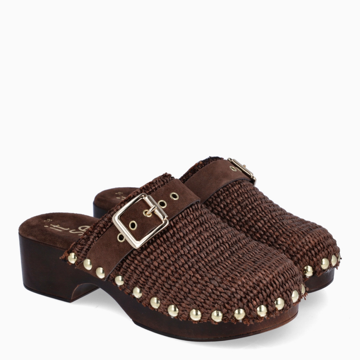 Zuecos de la marca Itse, modelo IVETTE. Zuecos elaborados en rafia trenzada color marrón oscuro con detalle de tachuelas y hebilla en pala. Interior en ante. Suela con tacón de 4cm de altura. Estos zuecos Itse IVETTE son un complemento ideal para llevar en el día a día!