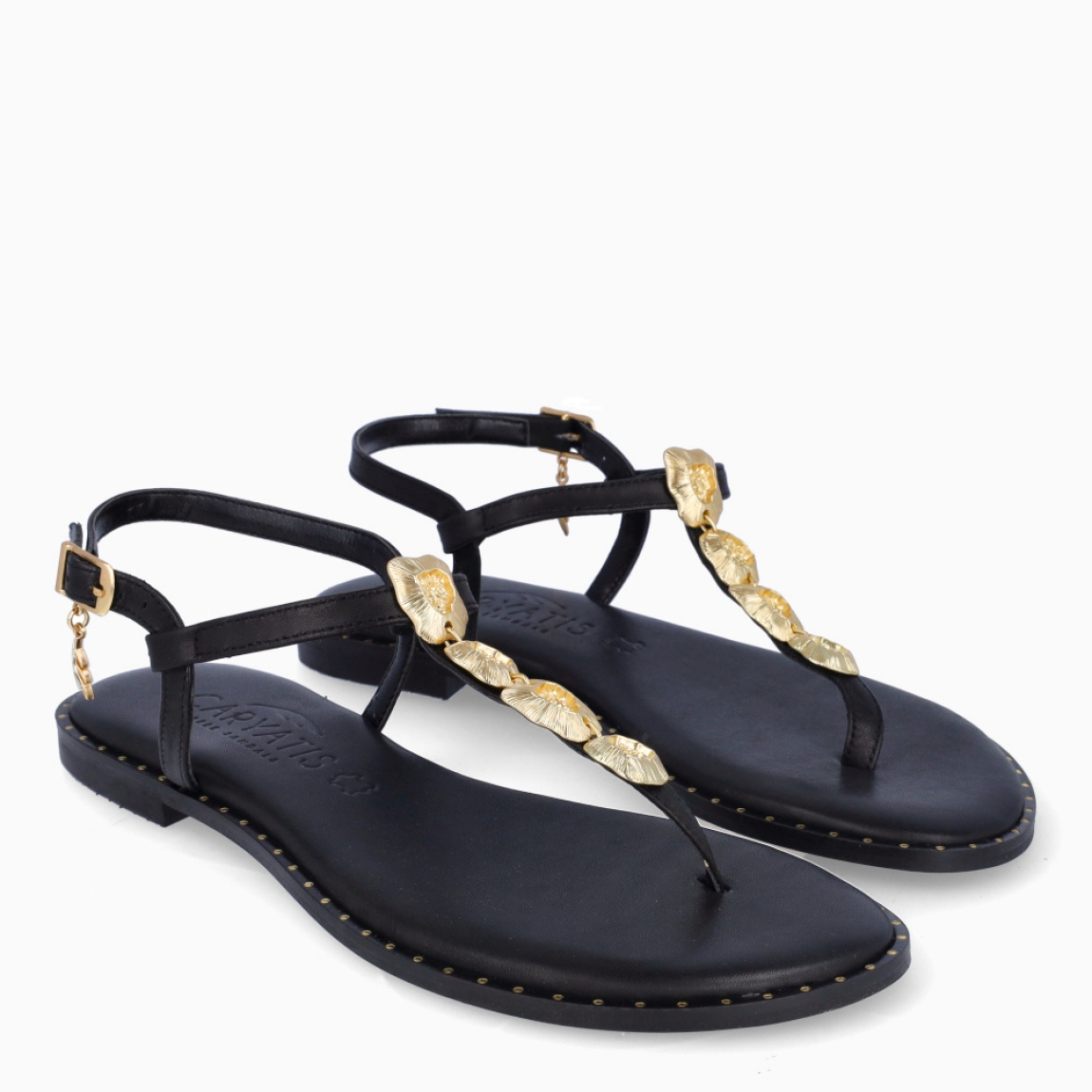 Esclavas de la marca Caryatis, modelo TILA. Exterior de las esclavas en piel color negro con adornos brillantes color oro. Cierre de las esclavas con hebilla y suela plana. Estas esclavas Caryatis TILA es un producto de alta calidad, pensado en la comodidad y elegancia. No puede faltar en tu armario de temporada.