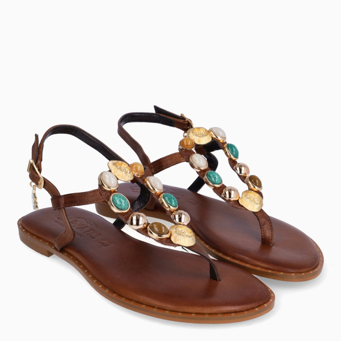 Esclavas de la marca Caryatis, modelo JAMILET. Exterior de las esclavas en piel color marrón con adornos en piedrería tonalidades marrones en pala. Cierre de las esclavas con hebilla y suela plana. Estas esclavas Caryatis JAMILET es un producto de alta calidad, pensado en la comodidad y elegancia. No puede faltar en tu armario de temporada.
