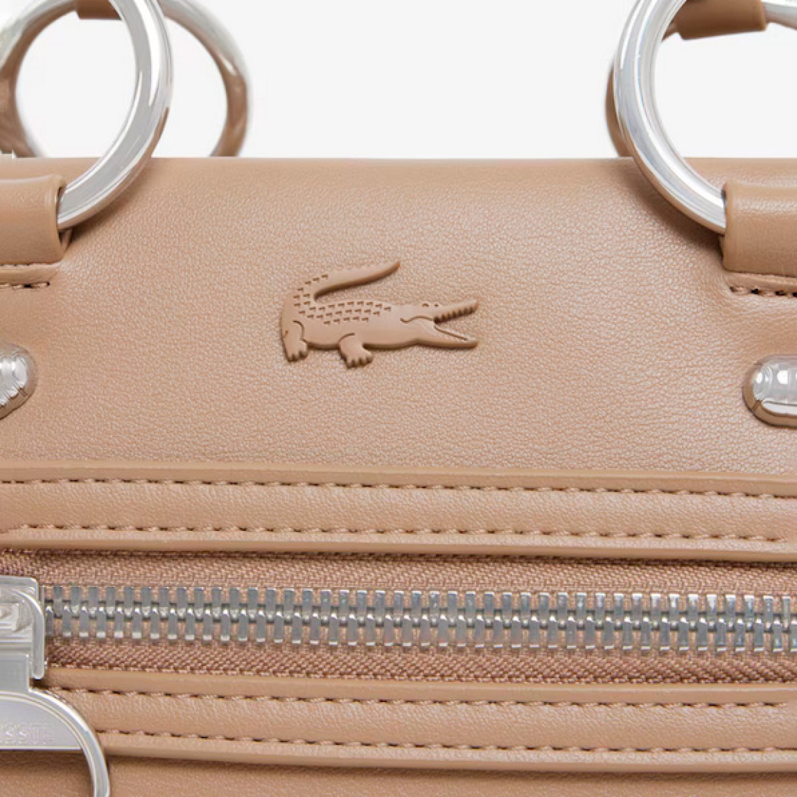 Bolso de la marca Lacoste, modelo CELYS. Elaborado en piel color taupe. Un bolso para llevar al hombro chic y desenfadado para hacer la transición del día a la noche con estilo. Su diseño intemporal incluye unos acabados sofisticados inspirados en el legado tenístico de Lacoste. Compacto, elegante y práctico, perfecto para usar a diario. Se adorna con un exclusivo cocodrilo metálico. Interior con bolsillo. Bolso para llevar al hombro o en bandolera, con Correa ajustable y amovible. Bolso Lacoste CELYS, ideal para llevarlo a todos lados! Medidas: alto 14cm y ancho 24cm.