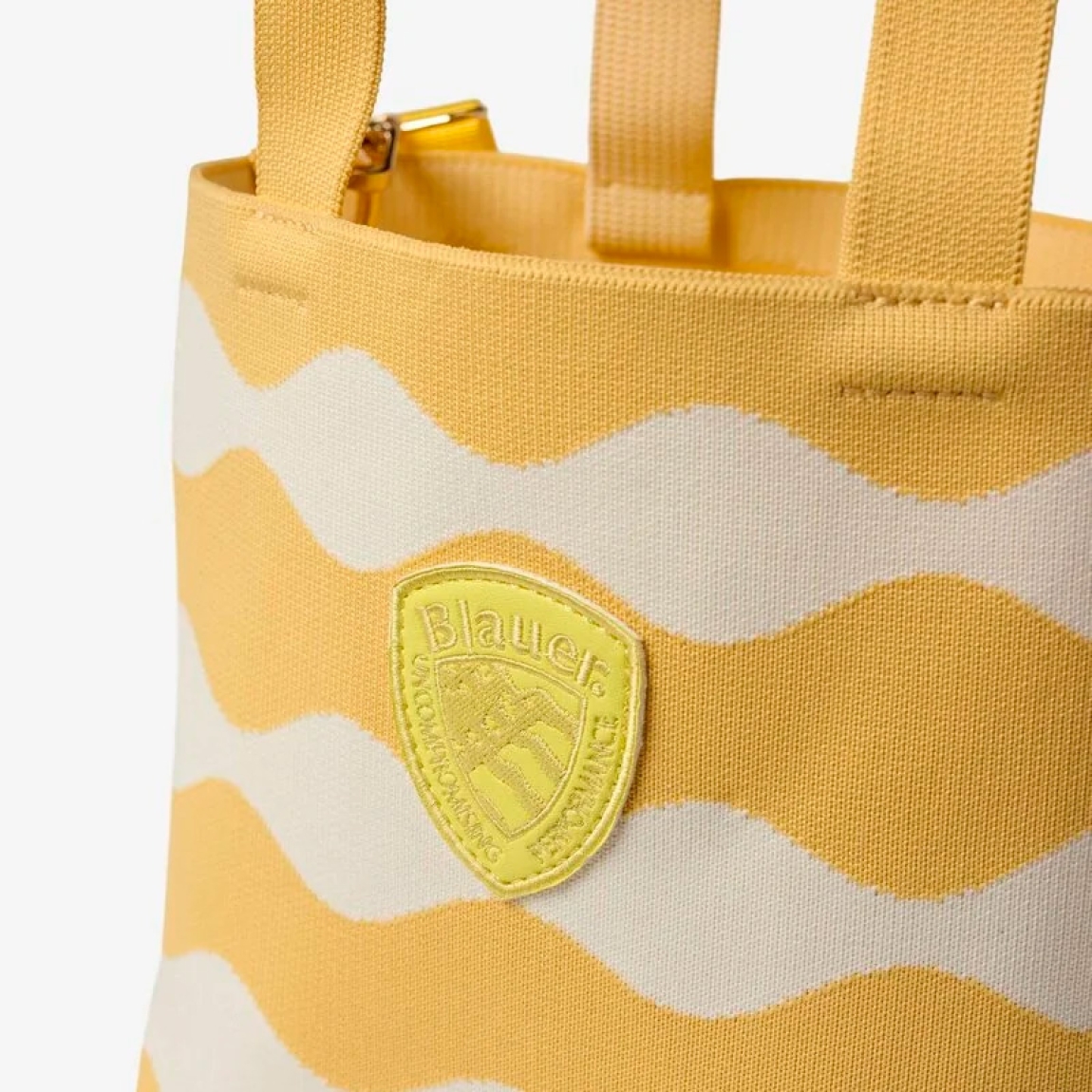Bolso de la marca Blauer, modelo BASK. Elaborado en tejido técnico color amarillo con un motivo de ondas, combina practicidad y un estilo contemporáneo. Bolso Blauer tipo canasta, es el accesorio ideal para la temporada de calor. Bolso Blauer dispone de dobles asas resistentes y el icónico escudo logotipado en el frontal. Ideal para el ocio o una jornada en la playa con un toque chic. Bolso Blauer BASK, ideal para llevar a todos lados! Medidas: 20 x 18 x 12cm.