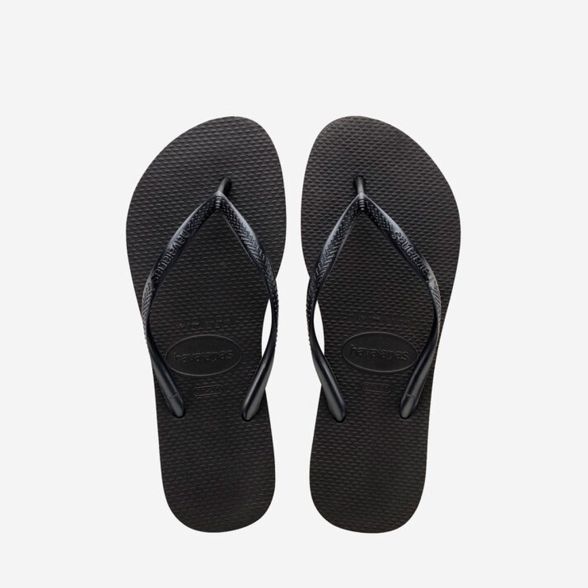Chanclas de la marca Havaianas, modelo SLIM FC. Chancas elaboradas en plástico color negro. Chanchas con ligereza, la suela de foma suave acompaña el pie sin pesar y el acabado antideslizante te da seguridad tanto en la arena como en el paseo de la tarde. El diseño se centra en estilizar el pie con unas tiras finas que aportan un brillo discreto y muy favorecedor. Cada detalle está pensado para que las chanclas Havaianas SLIM funcionen como una extensión natural de tu estilo: limpias, depuradas y con ese punto elegante que diferencia unas chanclas premium de unas básicas.