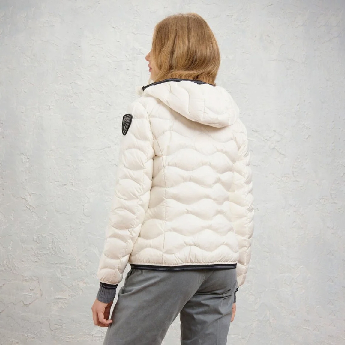 Chaqueta acolchada de la marca Blauer, modelo CAMELIA. Chaqueta con ondas horizontales de corte evasé. Esta prenda icónica de Blauer asegura un calor óptimo gracias al relleno natural de pluma (90/10 gr.165). Realizado en nylon brillante color blanco con forro en contraste, capucha fija y elástico rayado, se completa con un refinado parche con purpurina. Chaqueta Blauer CAMELIA, ideal para esta temporada!