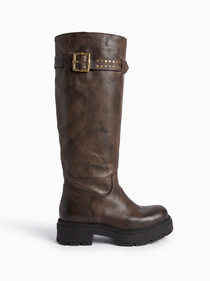 Botas altas de la marca Itse, modelo BALMA. Botas elaboradas en piel color taupe oscuro con hebilla y tachuelas en parte alta exterior. Botas sin cierre y con una punta redonda. Botas Itse con plataforma de 3cm de altura, que da una comodidad en cada paso. Botas Itse BALMA con un estilo moderno y contemporáneo, perfecto para usarlo con diferentes looks.