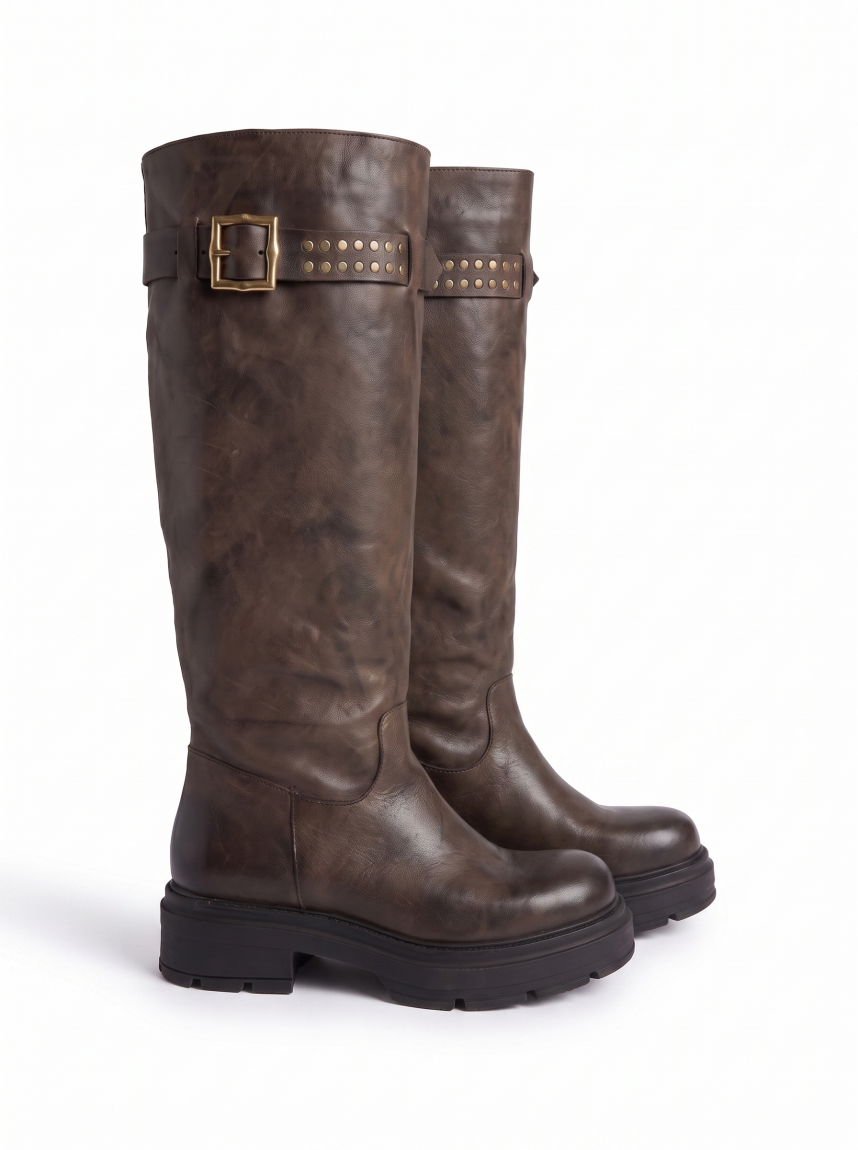Botas altas de la marca Itse, modelo BALMA. Botas elaboradas en piel color taupe oscuro con hebilla y tachuelas en parte alta exterior. Botas sin cierre y con una punta redonda. Botas Itse con plataforma de 3cm de altura, que da una comodidad en cada paso. Botas Itse BALMA con un estilo moderno y contemporáneo, perfecto para usarlo con diferentes looks.