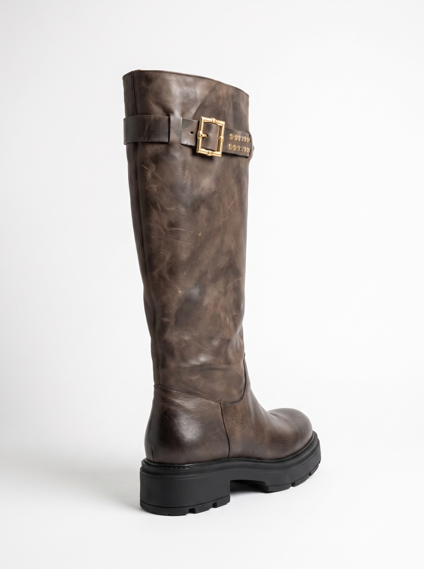 Botas altas de la marca Itse, modelo BALMA. Botas elaboradas en piel color taupe oscuro con hebilla y tachuelas en parte alta exterior. Botas sin cierre y con una punta redonda. Botas Itse con plataforma de 3cm de altura, que da una comodidad en cada paso. Botas Itse BALMA con un estilo moderno y contemporáneo, perfecto para usarlo con diferentes looks.