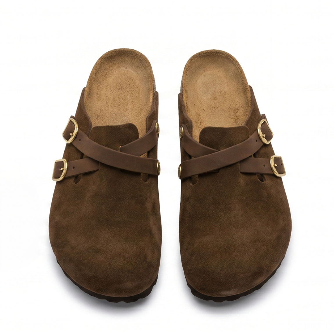 Zuecos de la marca Birkenstock, modelo BLAIR. Zuecos elaborados en piel de ante (serraje) color marrón chocolate, con detalle de tiras cruzadas en el empeine y elegantes hebillas ajustables en acabado dorado. Cuentan con la icónica plantilla anatómica de corcho y látex forrada en piel y suela plana de EVA ligera. Estos zuecos Birkenstock son ideales para complementar tus looks de temporada aunando tendencia y confort. No pueden faltar en tu armario.