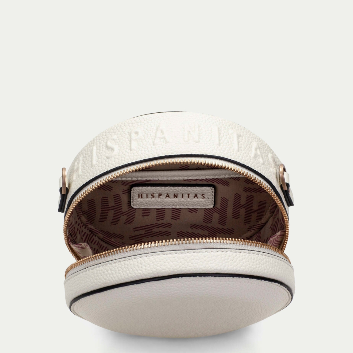 Bolso redondo de la marca Hispanitas, modelo OLGAT. Exterior del bolso en piel color blanco. Interior del bolso en textil color beig con estampado del logo de la marca. Cierre del bolso con cremallera y asa bandolera con estampado de marca extraíble y ajustable. Este bolso Hispanitas OLGAT es un complemento clásico con un diseño innovador y cómodo para tu día a día.