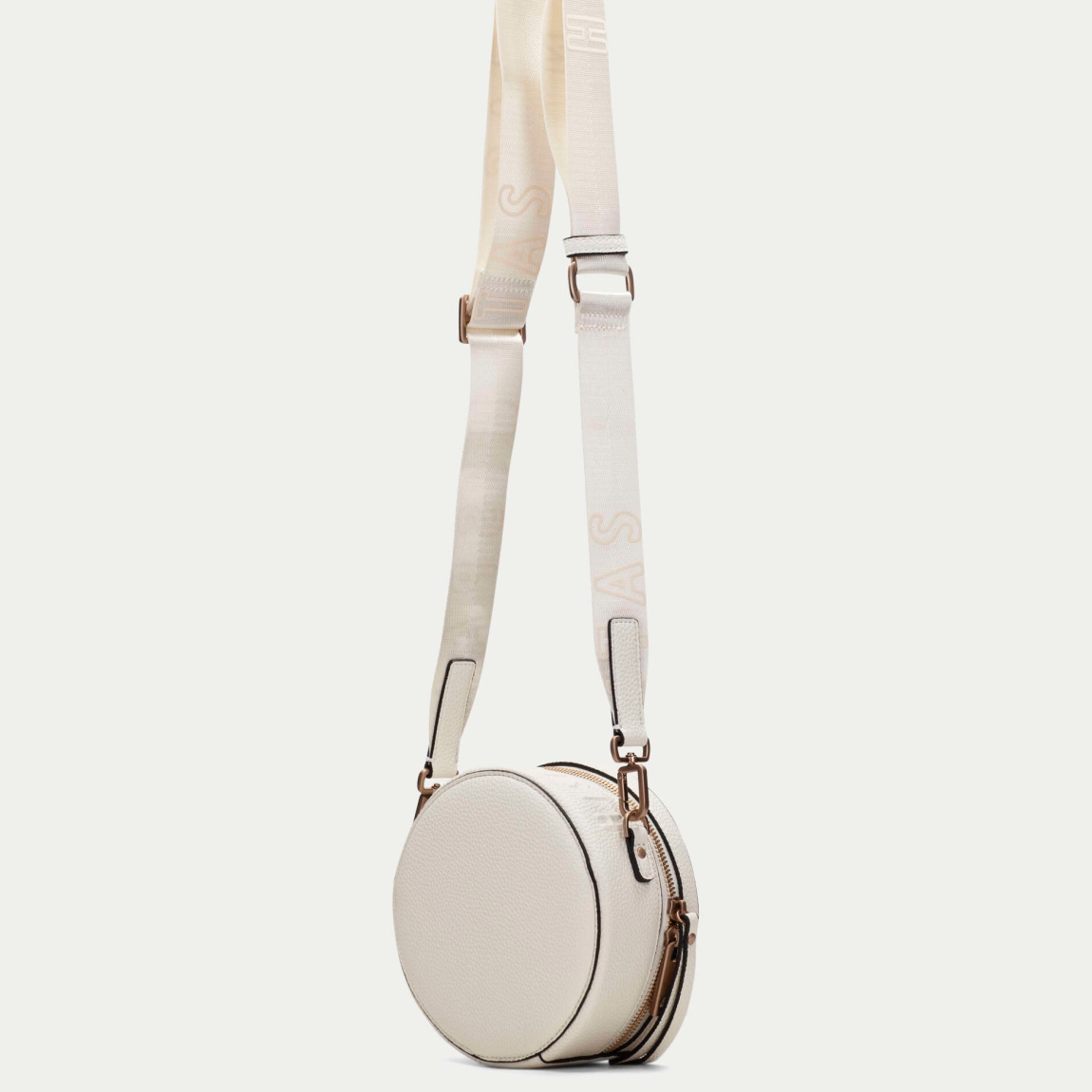 Bolso redondo de la marca Hispanitas, modelo OLGAT. Exterior del bolso en piel color blanco. Interior del bolso en textil color beig con estampado del logo de la marca. Cierre del bolso con cremallera y asa bandolera con estampado de marca extraíble y ajustable. Este bolso Hispanitas OLGAT es un complemento clásico con un diseño innovador y cómodo para tu día a día.