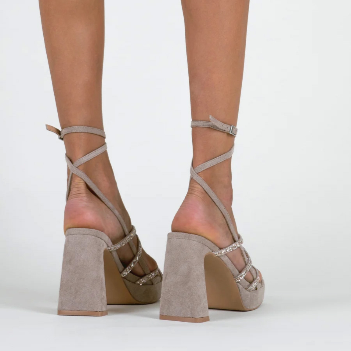 Sandalias de la marca Mim, modelo NORI. Exterior de las sandalias en ante color taupe compuesto con varias tiras con glitter a tono y dos tiras largas para atar en el tobillo. Interior de las sandalias en ante color taupe. Cierre de las sandalias Mim con hebilla y un tacón de 10cm de altura. Estas sandalias Mim NORI son ideales para tus eventos más importantes de temporada, te ayudarán a estilizar y crear diferentes looks con elegancia y estilo.