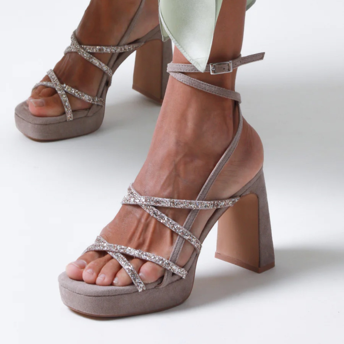 Sandalias de la marca Mim, modelo NORI. Exterior de las sandalias en ante color taupe compuesto con varias tiras con glitter a tono y dos tiras largas para atar en el tobillo. Interior de las sandalias en ante color taupe. Cierre de las sandalias Mim con hebilla y un tacón de 10cm de altura. Estas sandalias Mim NORI son ideales para tus eventos más importantes de temporada, te ayudarán a estilizar y crear diferentes looks con elegancia y estilo.