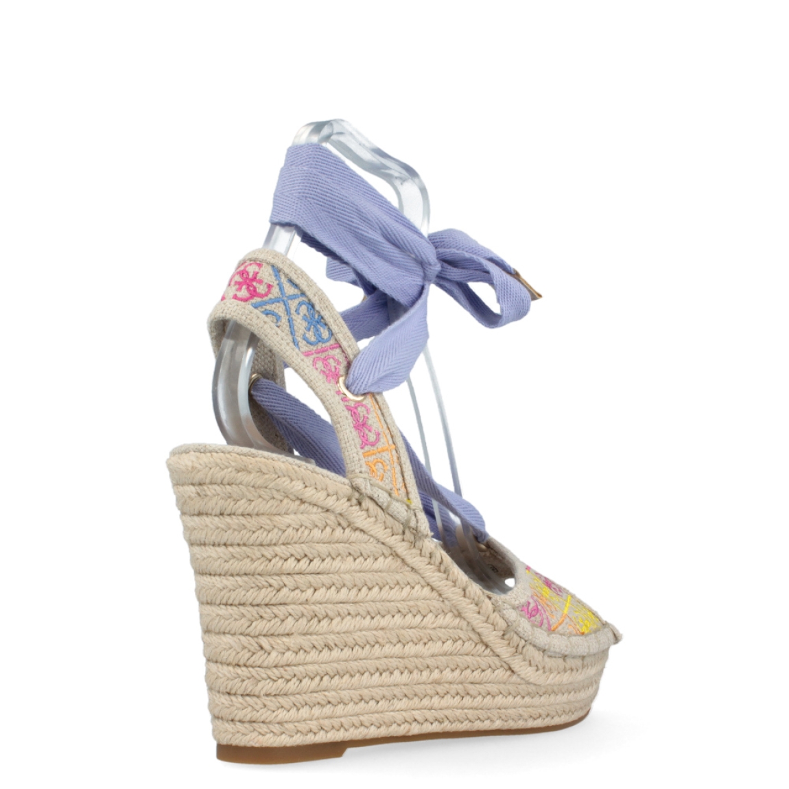 Sandalia multicolor de la marca Guess, modelo Halona. Exterior de la sandalia de tela de color beig, con logo 4G bordado multicolor. Interior de la sandalia de piel de color beig. Sandalia con lazo de color lila en el tobillo. Cierre de la sandalia con velcro y correa en el tobillo. Sandalia con suela de rafia de 10 cm de cuña, con 4 cm de plataforma. La sandalia Halona de Guess es ideal para dar un toque de color a tus looks.