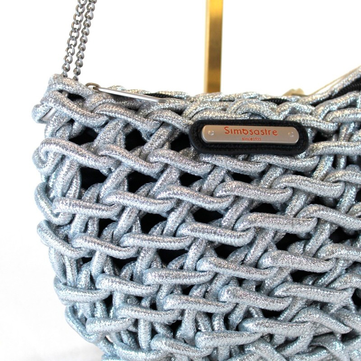 Bolso de la marca Simosastre, modelo JANETH. Bolso cruzado de cuerda elaborado en tela color plata con logo de acero en parte frontal. Cierre del bolso con cremallera y bandolera en metal en oro. Medidas del bolso:a lto 17cm y ancho 23cm. Este bolso Simosastre JANETH es un complemento ieal para darle estilo y personalidad a tus looks de temporada.