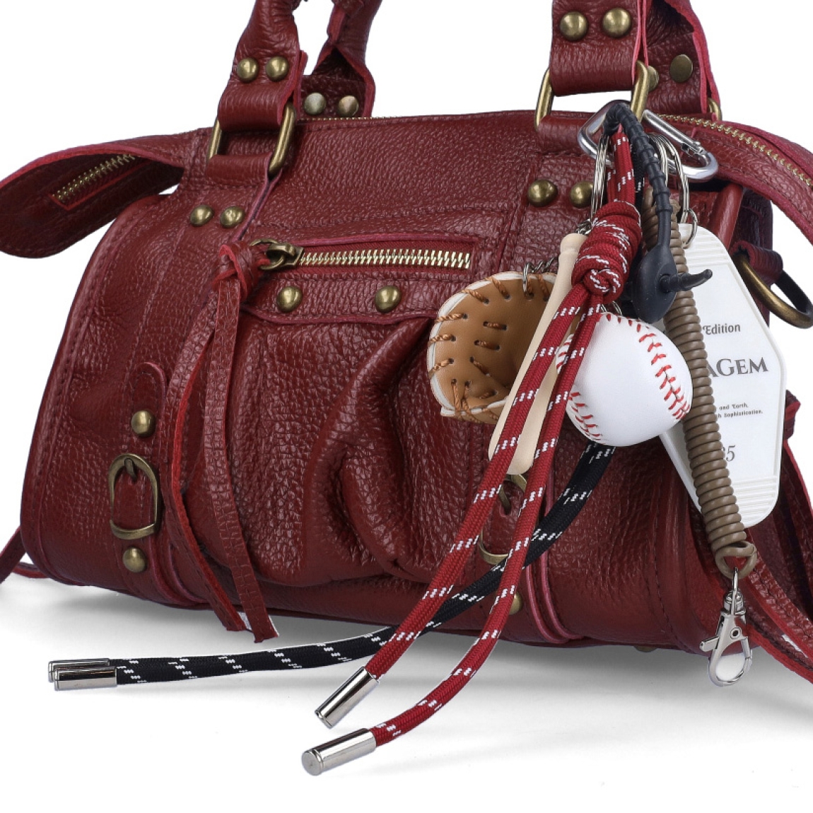 Charm de la marca MUNNÉ, modelo BÉISBOL. Formado por mini accesorios que aportan personalidad al bolso que lo añadas. Continee mini bate de béisbol, guante y pelota de béisbol, mosquetón en formade corazón, cuerda con nudo burdeos y negra, mosquetón con resorte marrón y placa con mensaje. Complemento perfecto para tus bolsos.
