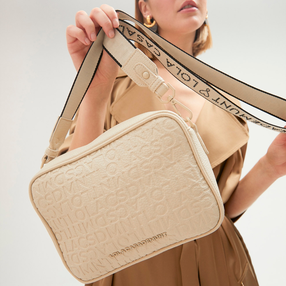 Bolso de la marca Lola Casademunt, modelo GEMMA. Bolso Bandolera con grabado monograma en efecto piel color beig. Contiene asa bandolera con detalle de logo en strass. Cierre con cremallera.ALTO: 25 cm - LARGO: 17 cm - ANCHO: 8 cm / BANDOLERA: 126 cm