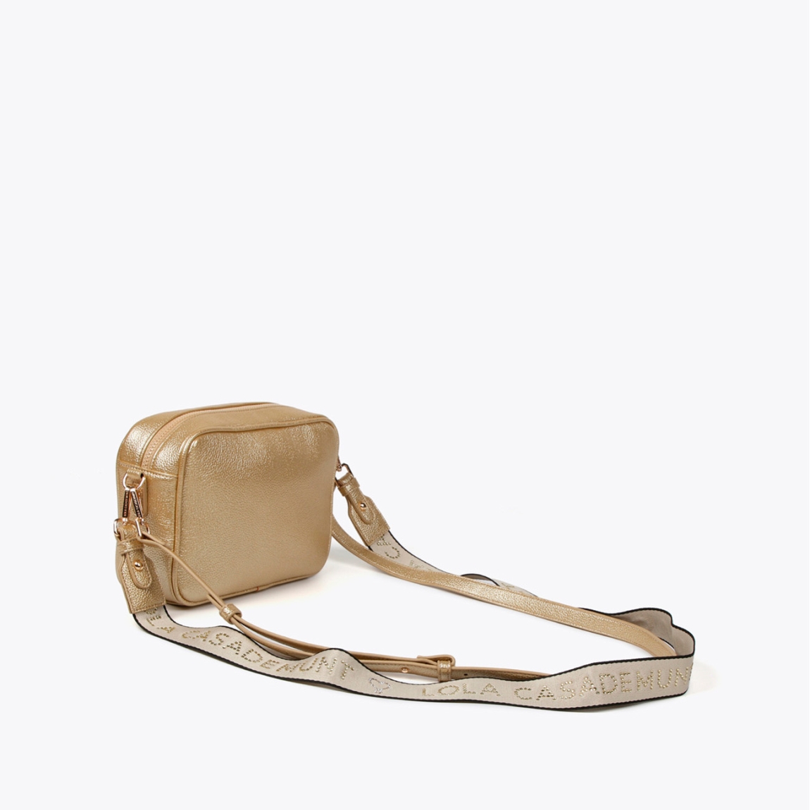 Bolso de la marca Lola Casademunt, modelo NORA. Bolso bandolera en efecto piel metalizado color oro. Detalle de grabado monograma. Contiene asa bandolera ajustable. Cierre con cremallera.ALTO: 25 cm - LARGO: 17 cm - ANCHO: 8 cm / BANDOLERA: 126 cm