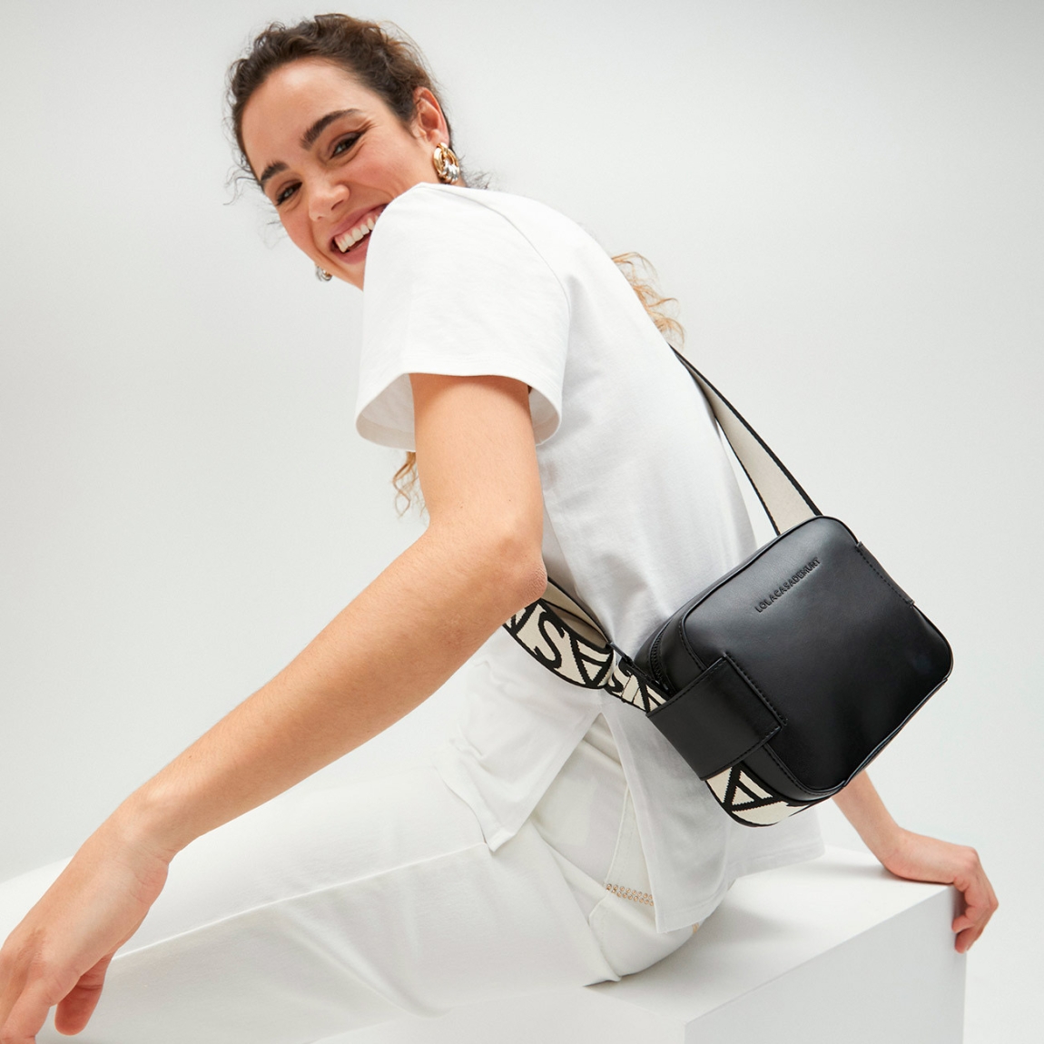 Bolso de la marca Lola Casademunt, modelo NOA. Bolso bandolera elaborado en piel color negro con logo de la marca en la parte frontal. Cuenta con compartimento interior amplio y un bolsillo interior. Cierre con cremallera y asa extraíble con estampado de la marca en negro y blanco. Medidas del bolso: alto 14cm y ancho 18cm. Este bolso Lola Casademunt NOA es un clásico, con un estilo versátil y atemporal. Perfecto para combinarlo con todos tus looks!