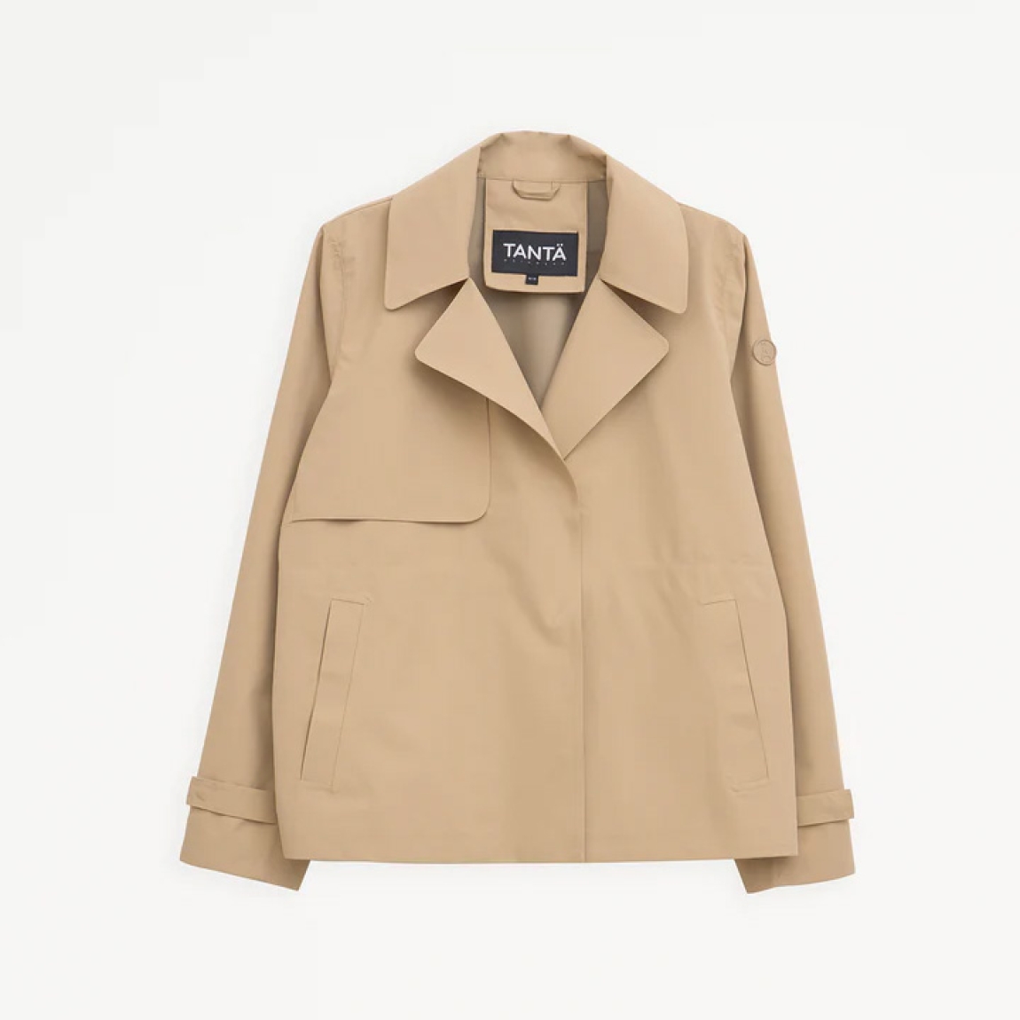 El trench o gabardina corta impermeable de la marca Tanta, modelo NIWL está cofeccionado en tejido de sarga de poliéster color camel. Es 100% impermeable y cuenta con todas las costuras selladas para una protección superior.Los detalles de la prenda incluyen un canesú en la espalda y otro en el lado derecho de la parte delantera, botones a presión ocultos y una capucha desmontable con cordón ajustable. Diseñado con un corte impecable, el modelo Niwl combina elegancia con una alta funcionalidad.