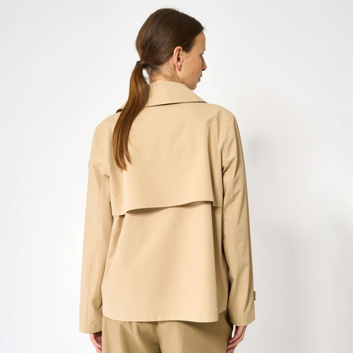 El trench o gabardina corta impermeable de la marca Tanta, modelo NIWL está cofeccionado en tejido de sarga de poliéster color camel. Es 100% impermeable y cuenta con todas las costuras selladas para una protección superior.Los detalles de la prenda incluyen un canesú en la espalda y otro en el lado derecho de la parte delantera, botones a presión ocultos y una capucha desmontable con cordón ajustable. Diseñado con un corte impecable, el modelo Niwl combina elegancia con una alta funcionalidad.