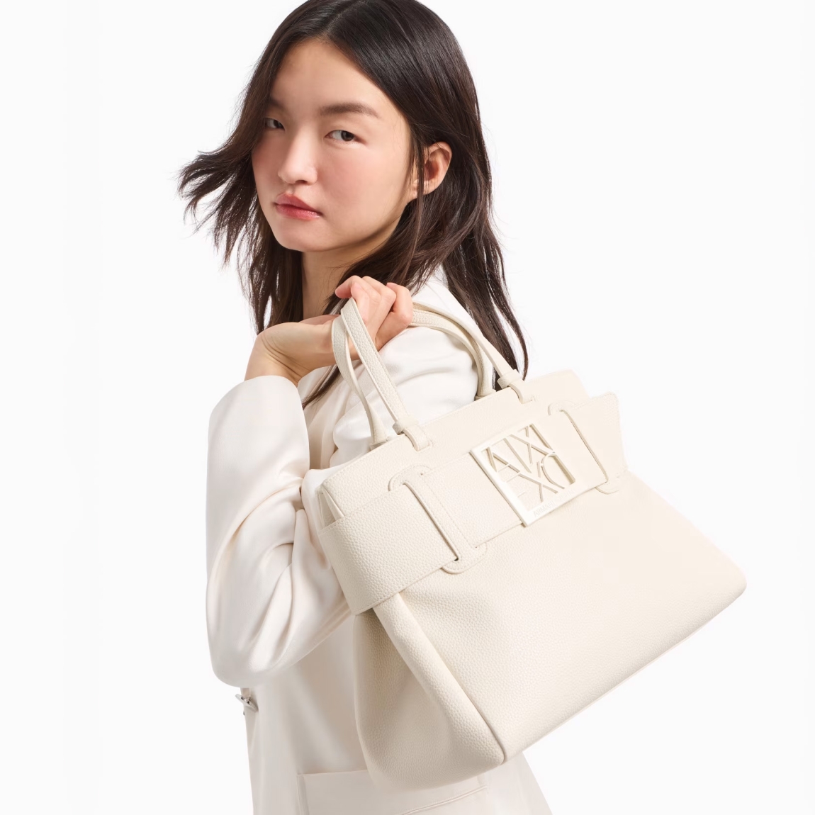 Bolso de mano de la marca Armani Exchange, modelo SOPHI. Elaborado en piel sintética color blanco, elegante y práctico, ideal para cualquier ocasión. El detalle del logotipo tonal en la parte delantera añade un toque sutil de sofisticación. El cierre magnético garantiza seguridad y facilidad de uso, mientras que las dos asas ofrecen un agarre cómodo para un transporte versátil. En el interior, un bolsillo adicional te permite organizar mejor tus artículos personales. Perfecto para el uso diario, este bolso combina estilo, funcionalidad y atención al detalle. Medidas: alto 24cm y ancho 30cm.