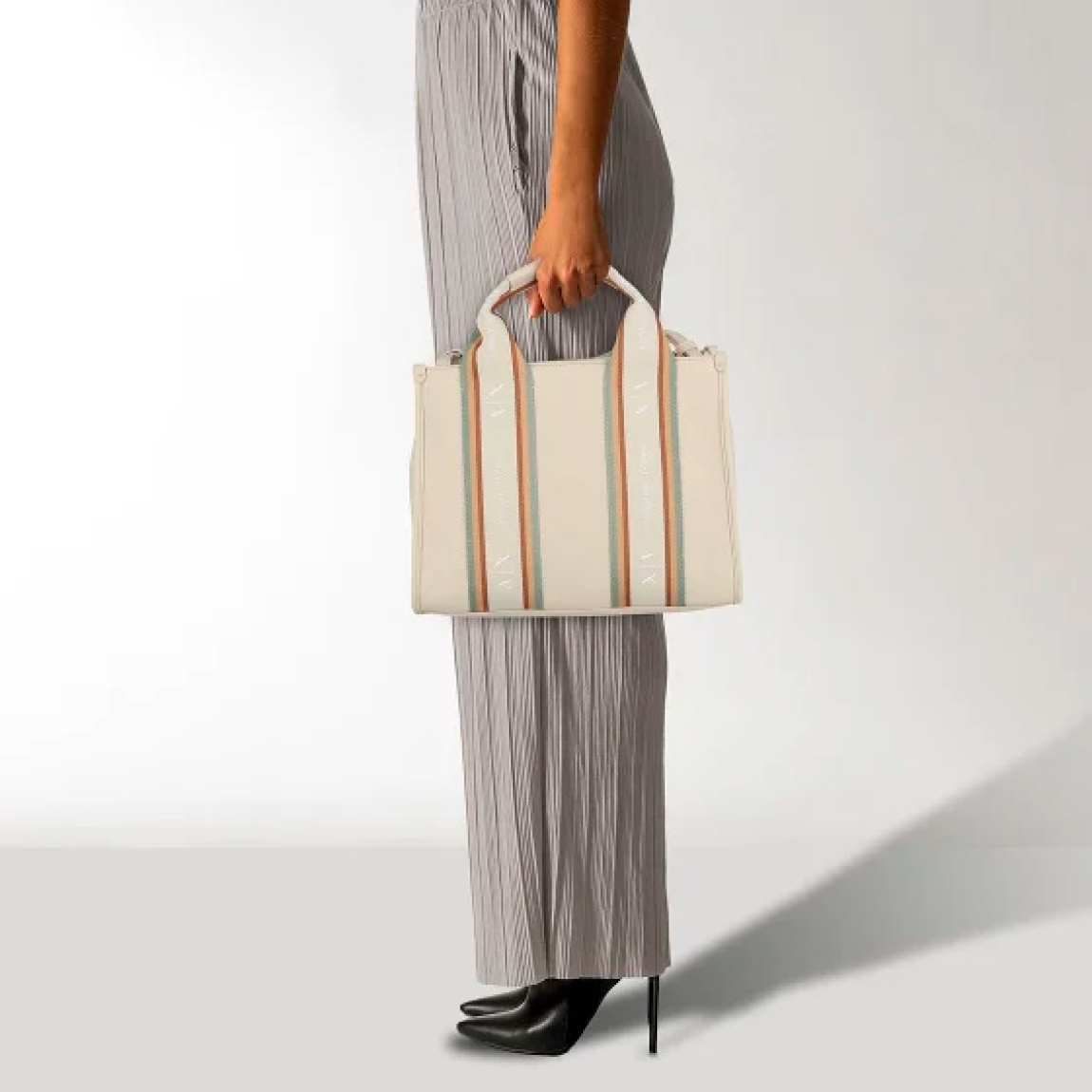Bolso de la marca Armani Exchange, modelo VALLEY. Elaborado en piel color beig con rayas multicolor y estampado de marca. Cierre con cremallera, asas fijas y extraíbles. Incluye un práctico compartimento para el teléfono móvil, bolsillos interiores y un compartimento con cremallera de fácil acceso, cuyo cierre permite abrirlo y cerrarlo sin esfuerzo. Este elegante acompañante es perfecto para las amantes de la moda. Medidas: altura 22cm y ancho 29cm. Complemento resistente, este bolso Armani Exhchange promete durabilidad y robustez sin renunciar a la elegancia.