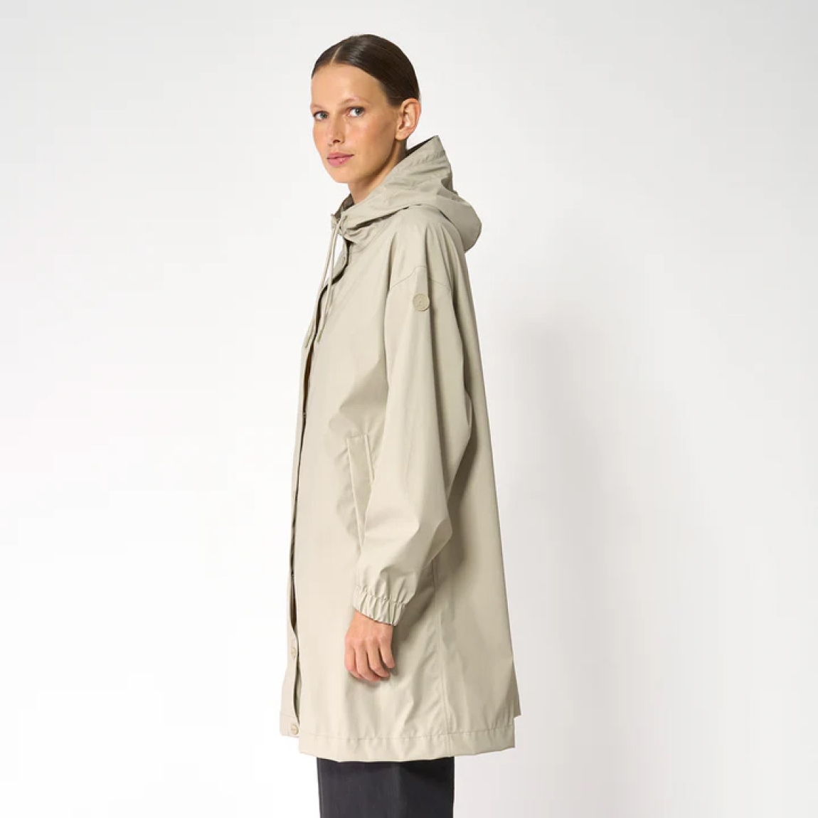 Chaqueta impermeable de la marca Tanta, modelo Mis. Es un chubasquero de corte holgado y diseño siempre contemporáneo 100% impermeable. Está confeccionada con un tejido ligero de PU color beig y cuenta con todas las costuras selladas para una protección superior. Los detalles de la prenda incluyen botones a presión, una capucha con visera incorporada y bolsillos con ribetes. Ideal para esta temporada!