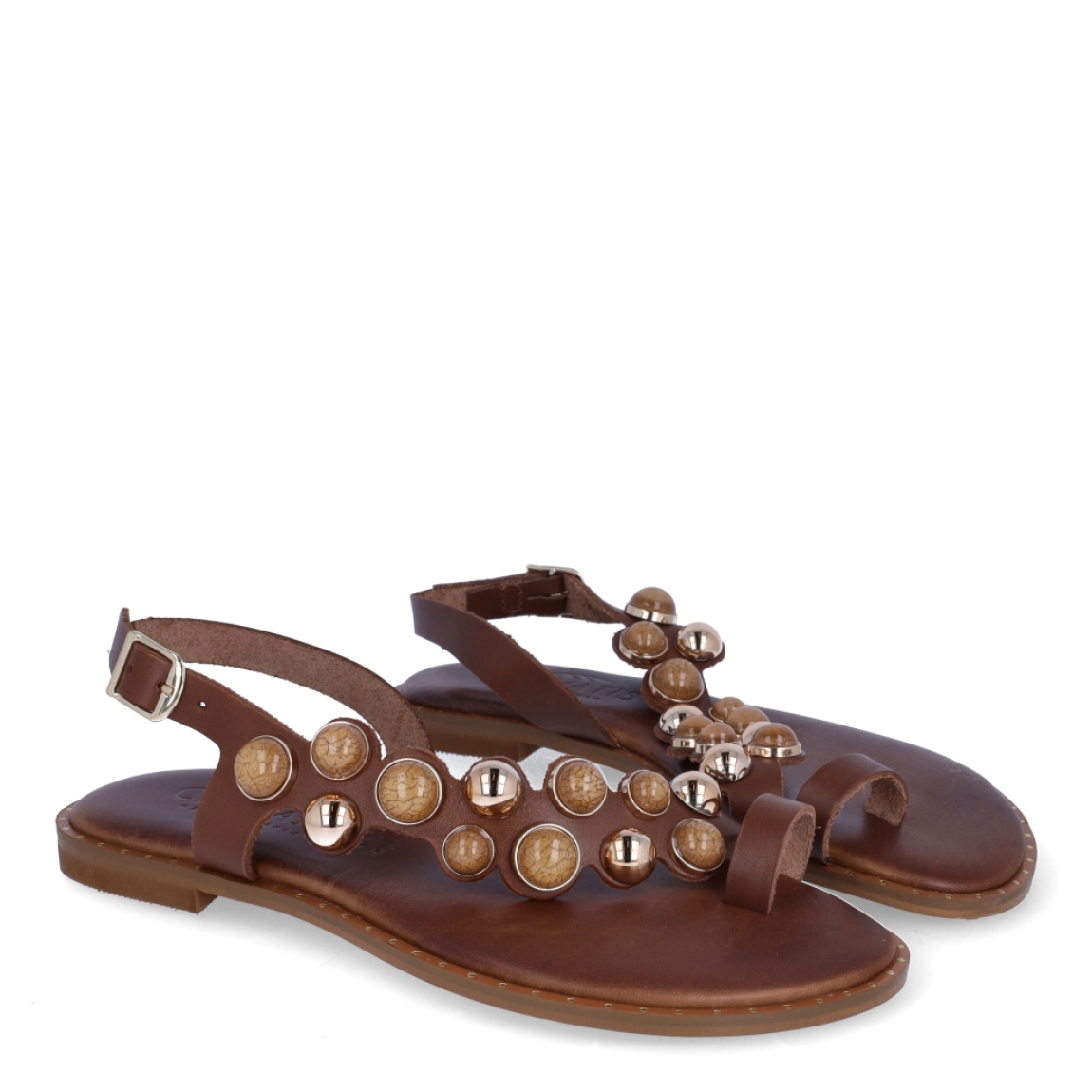 Esclavas de la marca Caryatis, modelo SENDRA. Exterior de las esclavas en piel color marrón con adornos en piedrería. Cierre de las esclavas con hebilla y suela plana. Estas esclavas Caryatis SENDRA es un producto de alta calidad, pensado en la comodidad y elegancia. No puede faltar en tu armario de temporada.