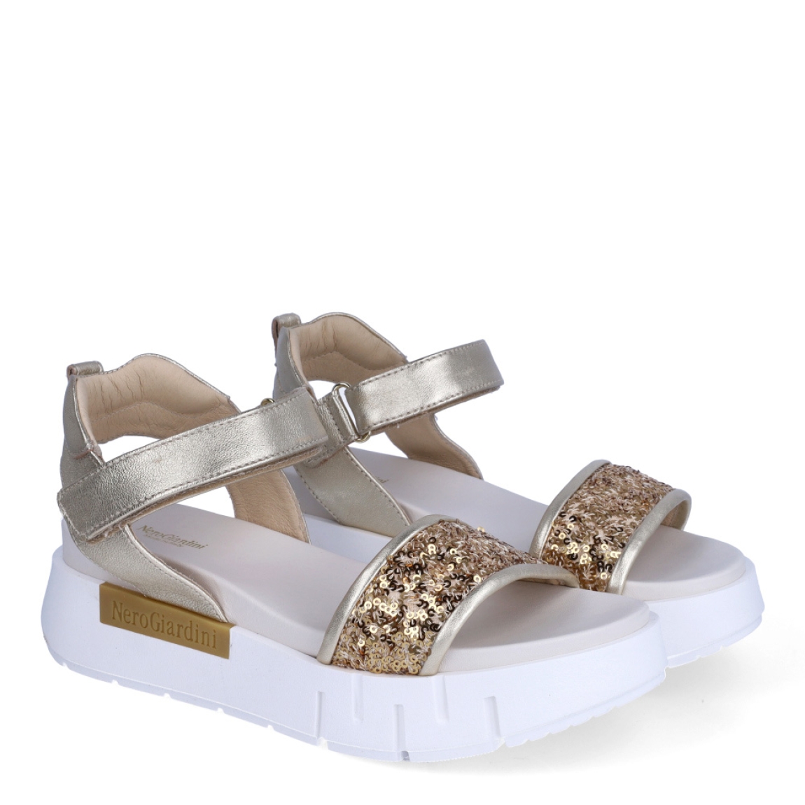 Sandalias de la marca Nerogiardini, modelo JESS. Exterior de las sandalias en piel color platino con detalle de lentejuelas color dorado en la pala. Interior de las sandalias en piel color blanco. Cierre de las sandalias Nerogiardini con velcro. Sandalias con plataforma de 4cm de altura. Estas sandalias Nerogiardini JESS son un complemento clásico, inspirado en la comodidad, ligereza que necesitas en tu día a día.