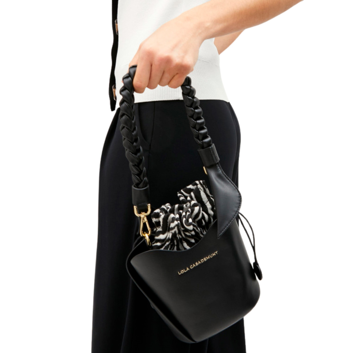 Bolso de la marca Lola Casademunt, modelo BOMB. Exterior en piel color negro con asa corta trenzada. Incluye saco interior con estampado cebra, asa larga y cierre ajustable con cordón. Medidas alto 18cm y ancho 18cm. Este bolso Lola Casademunt BOMB es ideal para llevarlo a todos lados!
