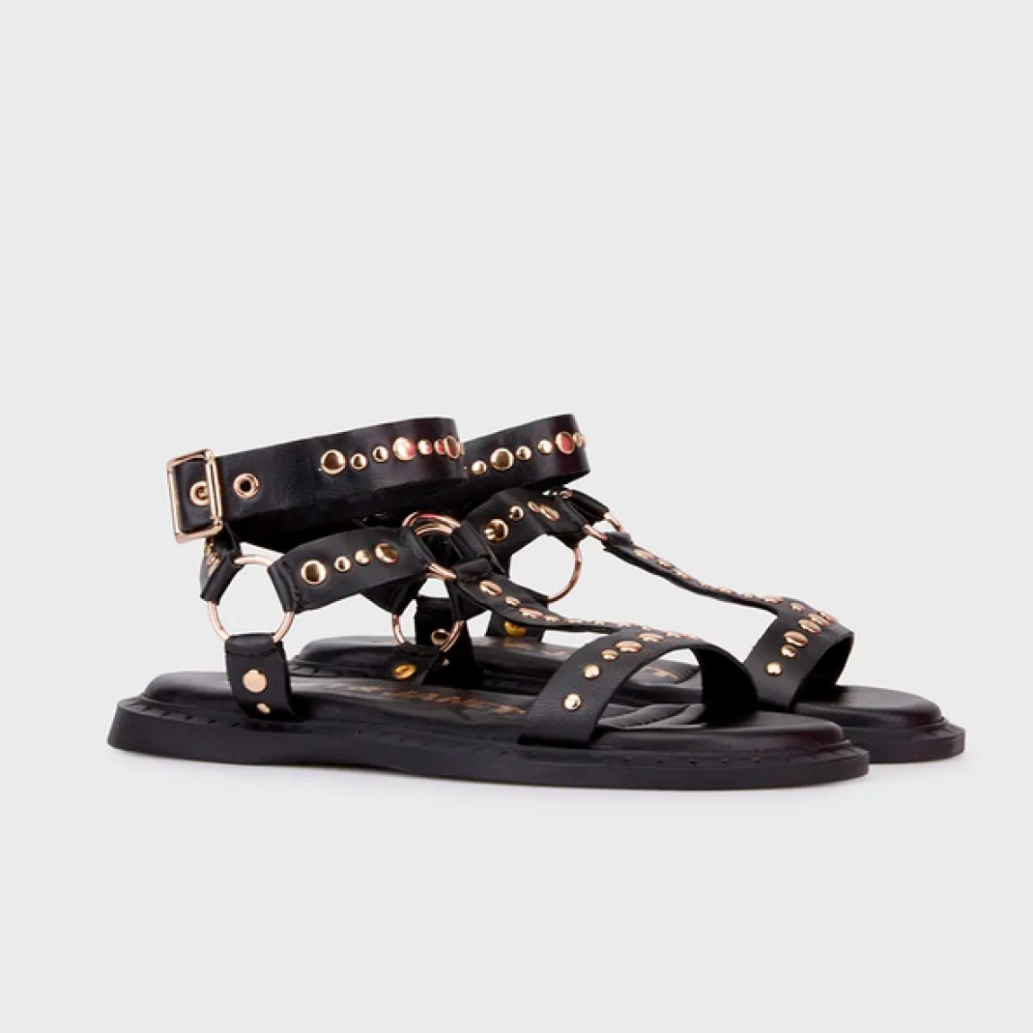 Sandalias de la marca Janet & Janet, modelo SASHA. Exterior en piel color negro con detalle de tachuelas doradas en tiras. Interior en piel color negro con estampado de logo marca. Cierre con hebilla. Suela de sandalias de goma y plana. Estas sandalias Janet & Janet tienen un diseño auténtico, que hará destacar tus looks a donde vayas!